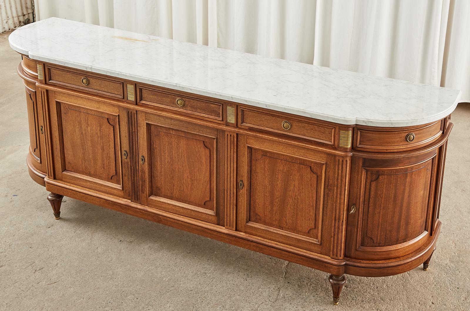 Grand French mahogany sideboard server or buffet featuring a 1 inch thick Cararra marble slab top with a conforming ogee edge. Beautifully crafted in the French Louis XVI neoclassical taste embellished with bronze mounts. The case has gracefully