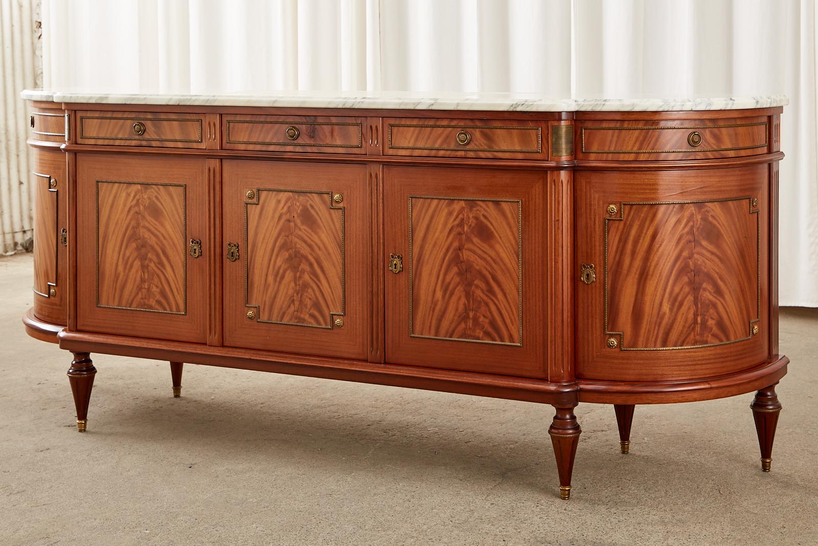 Grand French mahogany sideboard server or buffet featuring a 1 inch thick Carrara marble slab top with a conforming ogee edge. Crafted in the neoclassical Louis XVI taste with bronze mounts. The case is constructed with radiant mahogany and features