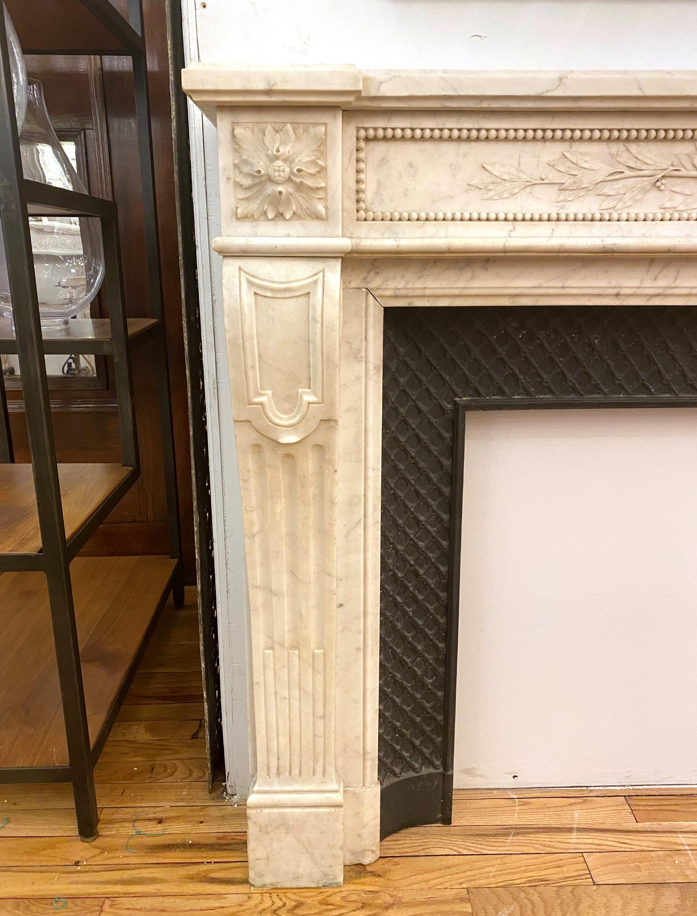 Louis XVI French white marble mantel with a cast iron insert. The breast of the mantle is decorated with a carved center wreath and foliage, framed by a beaded border. Hearth not included. Please note, this item is located in one of our NYC