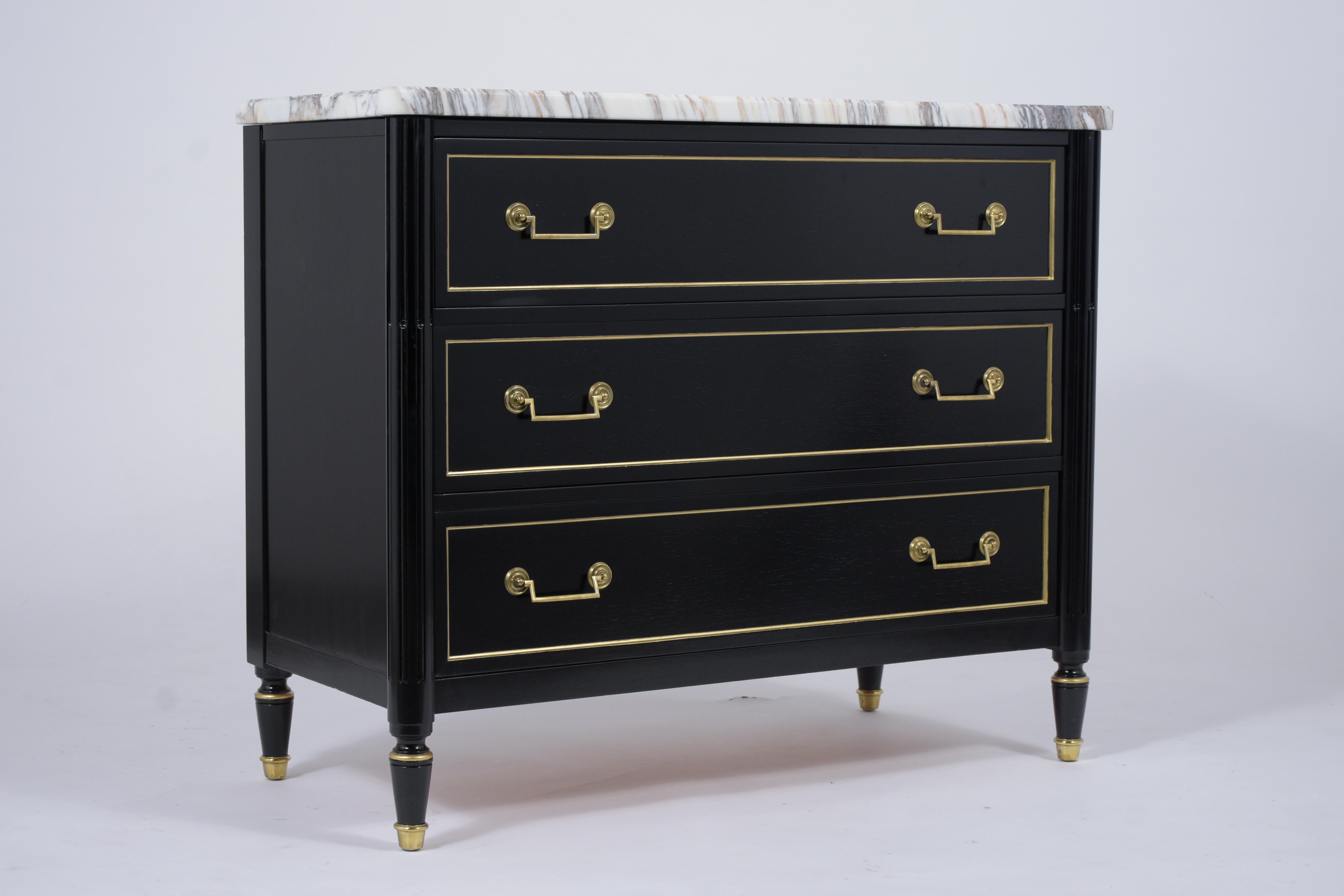 This elegant French Louis XVI ebonized commode is made out of mahogany wood and has a new ebonized lacquer finish. This antique dresser features a white Carrara marble with beveled edge details, three drawers framed by elegantly rounded giltwood