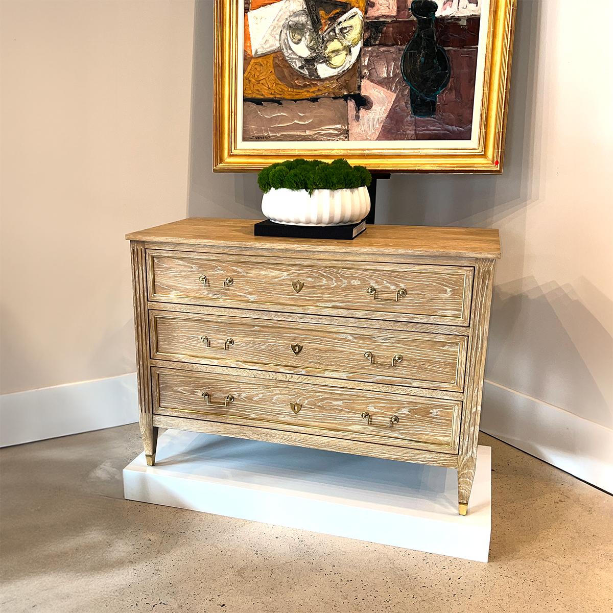Un comò in stile Neo Classico della fine del XVIII secolo. Con tre lunghi cassetti a chiusura ammortizzata con finitura impiallacciata in rovere naturale, fianchi rivestiti, accenti e ferramenta in ottone lucido, stili scanalati, gambe quadrate