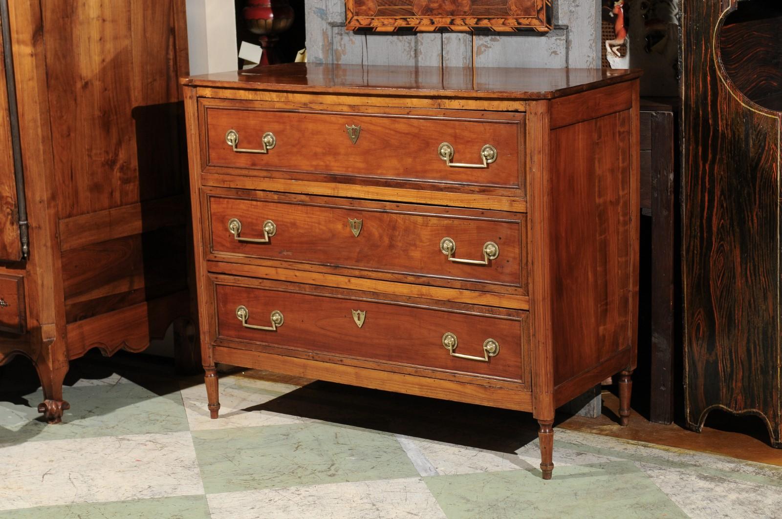 The French Louis XVI fruitwood commode with rectangular top, 3 drawers, rounded fluted corners ending in turned legs.