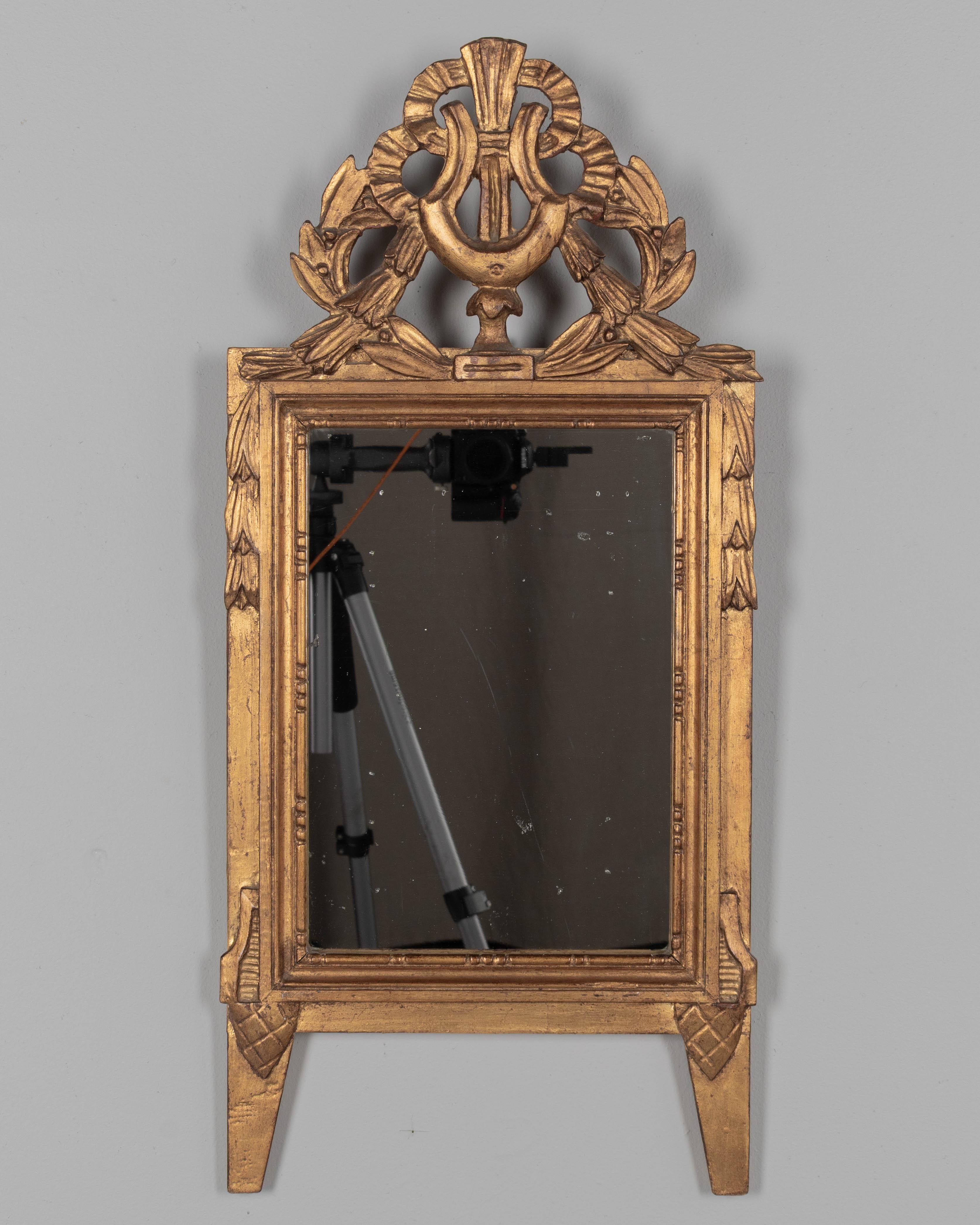 Espejo de madera dorada provenzal francesa de estilo Luis XVI. Cresta tallada a mano con cintas y guirnaldas. El espejo es original con plateado antiguo. En buen estado, con un cálido acabado dorado. No hay restauraciones. Alrededor de