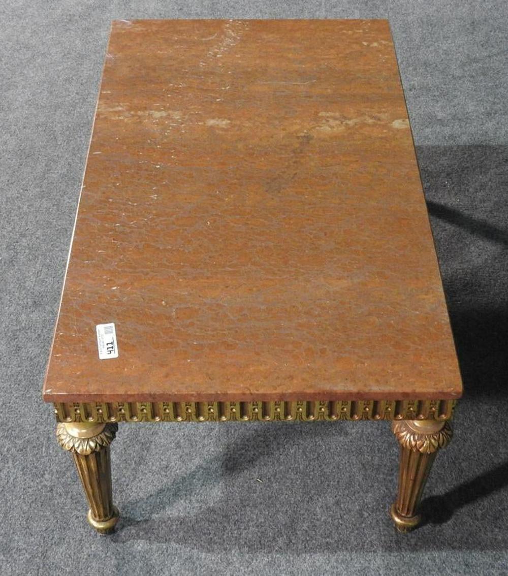 This is a beautifully designed French 1930s era coffee table. The table has a wonderful patina on its gilded surface and a great slab of rouge marble on top. The table has an older professional repair on the top and is missing a brass toe cap. We