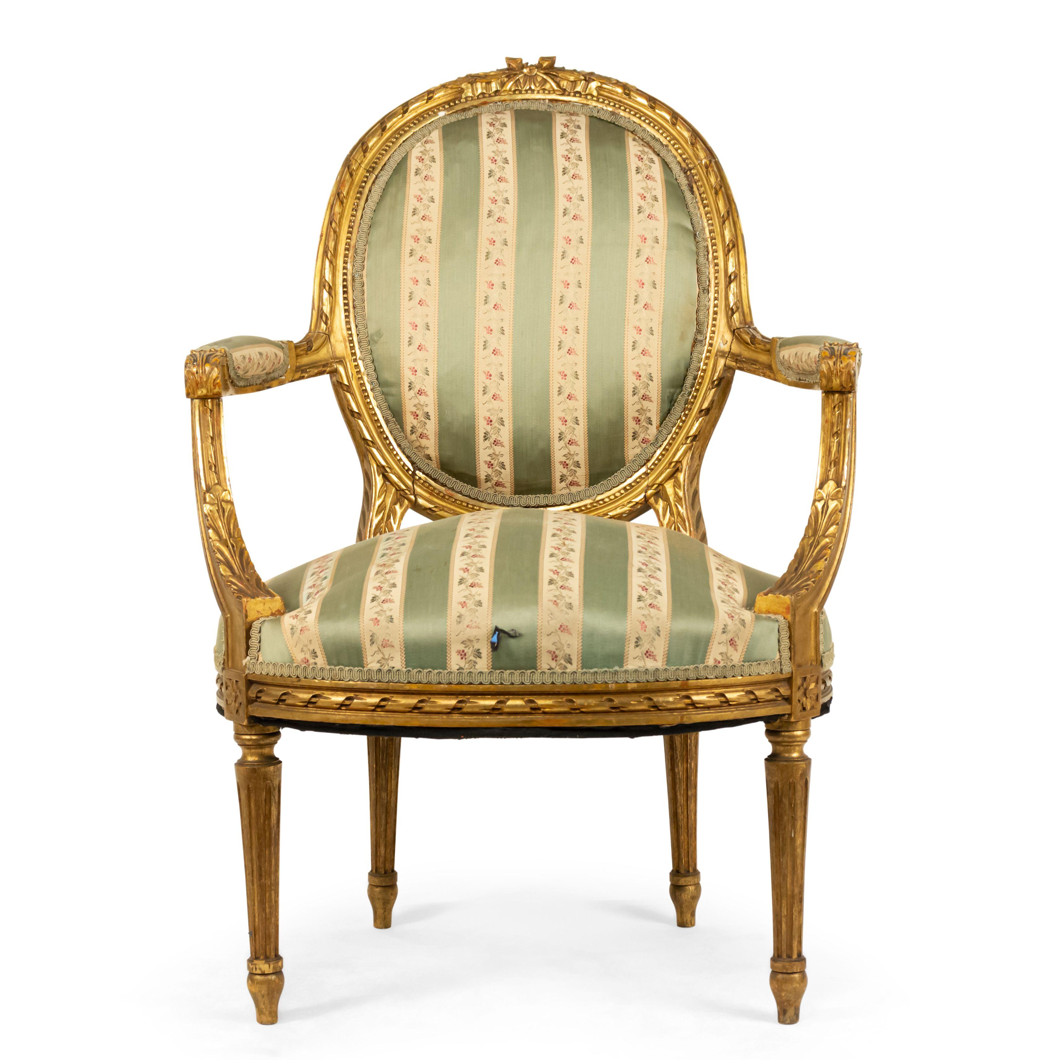 French Louis XVI style (19-20th century) gilt armchair with a carved oval back and green striped upholstery.