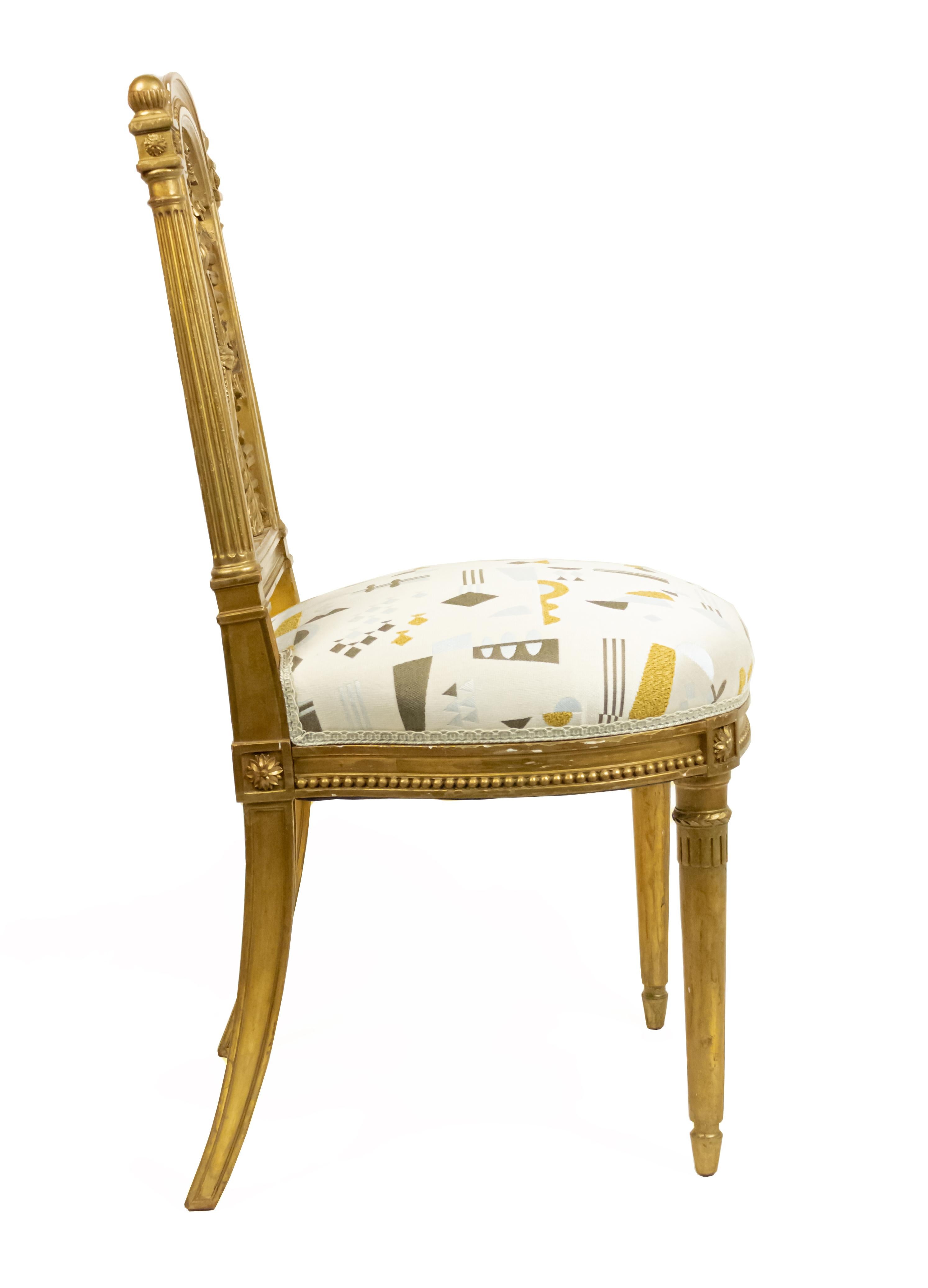 Pair of French Louis XVI style 19th century gilt side chairs with carved back designed with wreath and arrow and initials MA (Marie Antoinette) with contemporary off-white multicolored geometric upholstery.