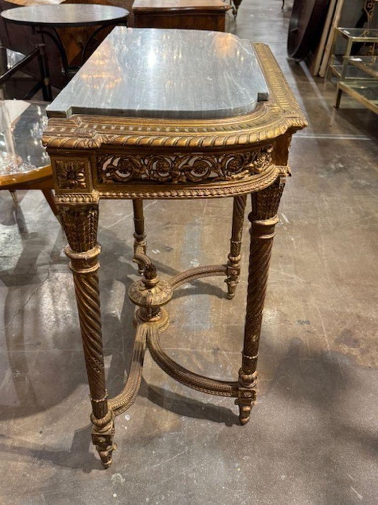 Consolle francese del XIX secolo dal design Luigi XVI, intagliata e dorata, con inserti in marmo grigio. Consolle francese di design Luigi XVI in legno intagliato e dorato con inserto in marmo grigio che fonde la simmetria neoclassica con l'opulenta