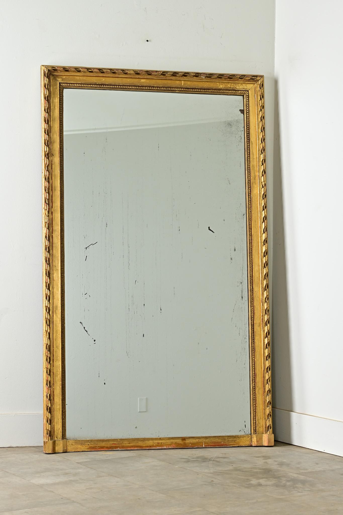 Die exquisit geschnitzte Bandleiste dieses Louis XVI-Spiegels hält die originale Spiegelplatte mit schillernder Kristallisierung und Stockflecken. Rotes Holz unter der Vergoldung verleiht dem wirbelnden Muster weitere Tiefe und Dimension, die sich