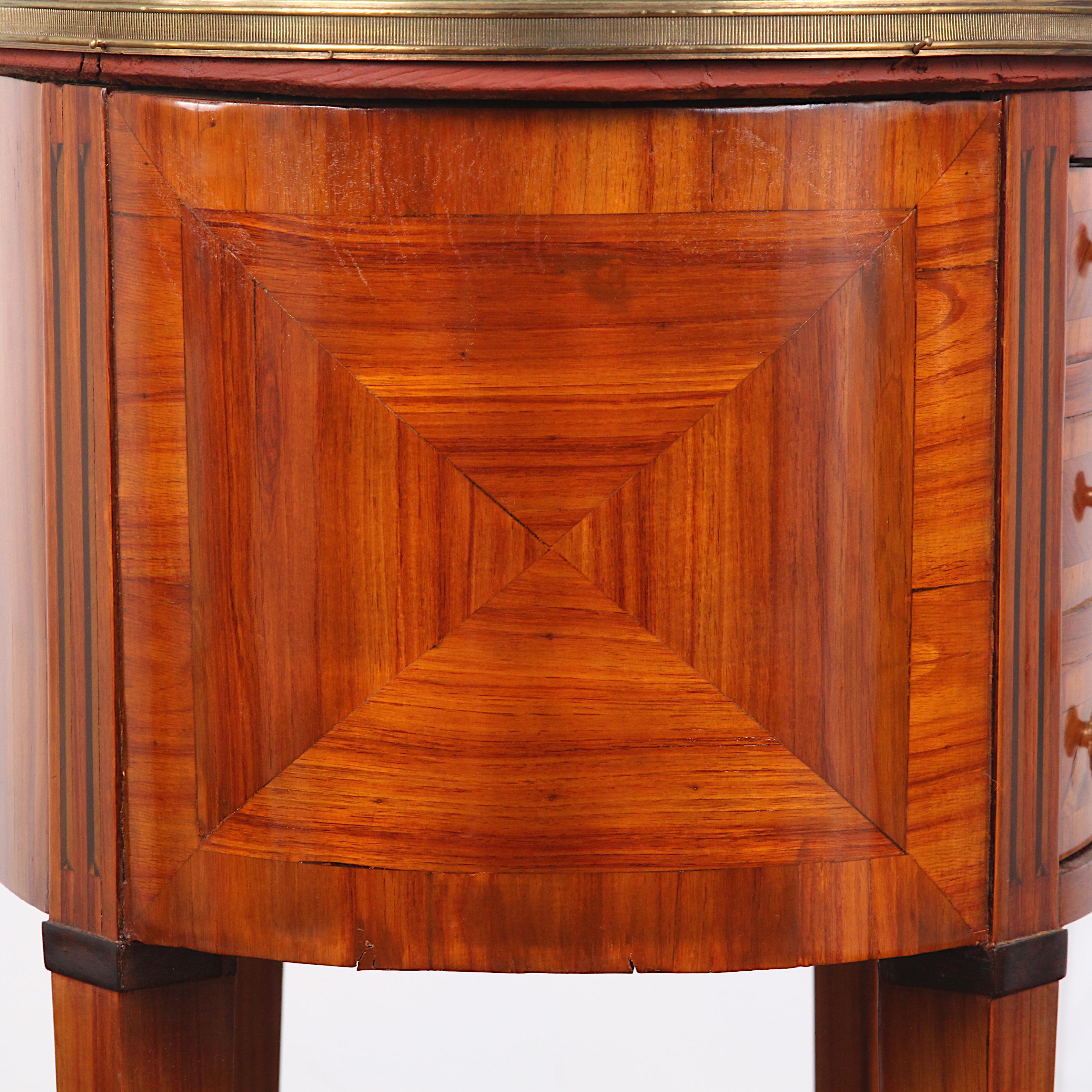 A lovely-quality French oval-shaped nightstand or side table, the sides and door front veneered and banded in kingwood, the oval top with pierced brass gallery, and with long square tapering legs with brass capped feet. The door front has three