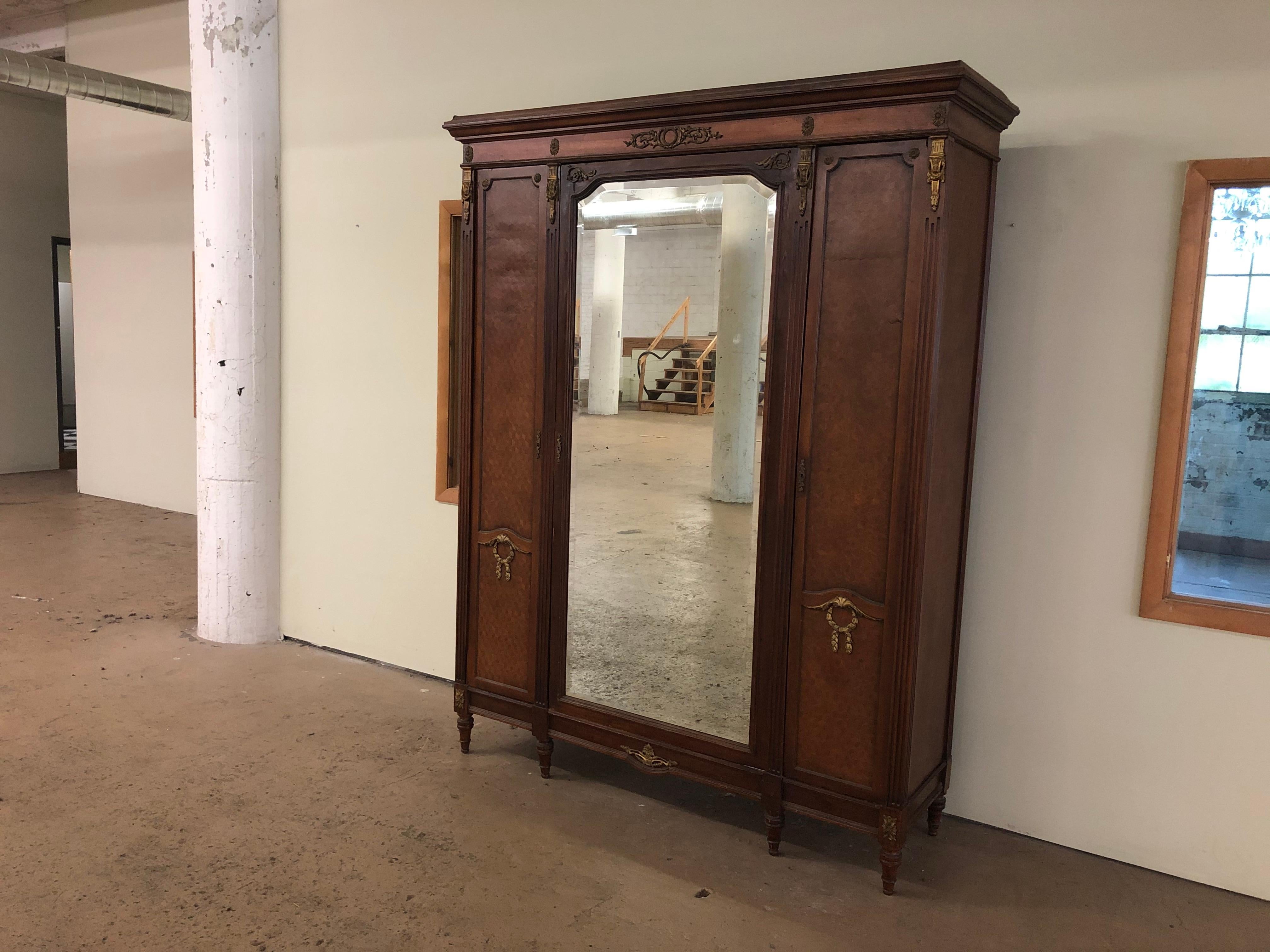 A stunning French Louis XVI knockdown armoire dresser or wardrobe

France, circa 1900

Mahogany and satinwood, with inlaid parquetry and mounted bronze ormolu. Beveled mirror on center door and mirrored interiors on side doors. Interior shelving
