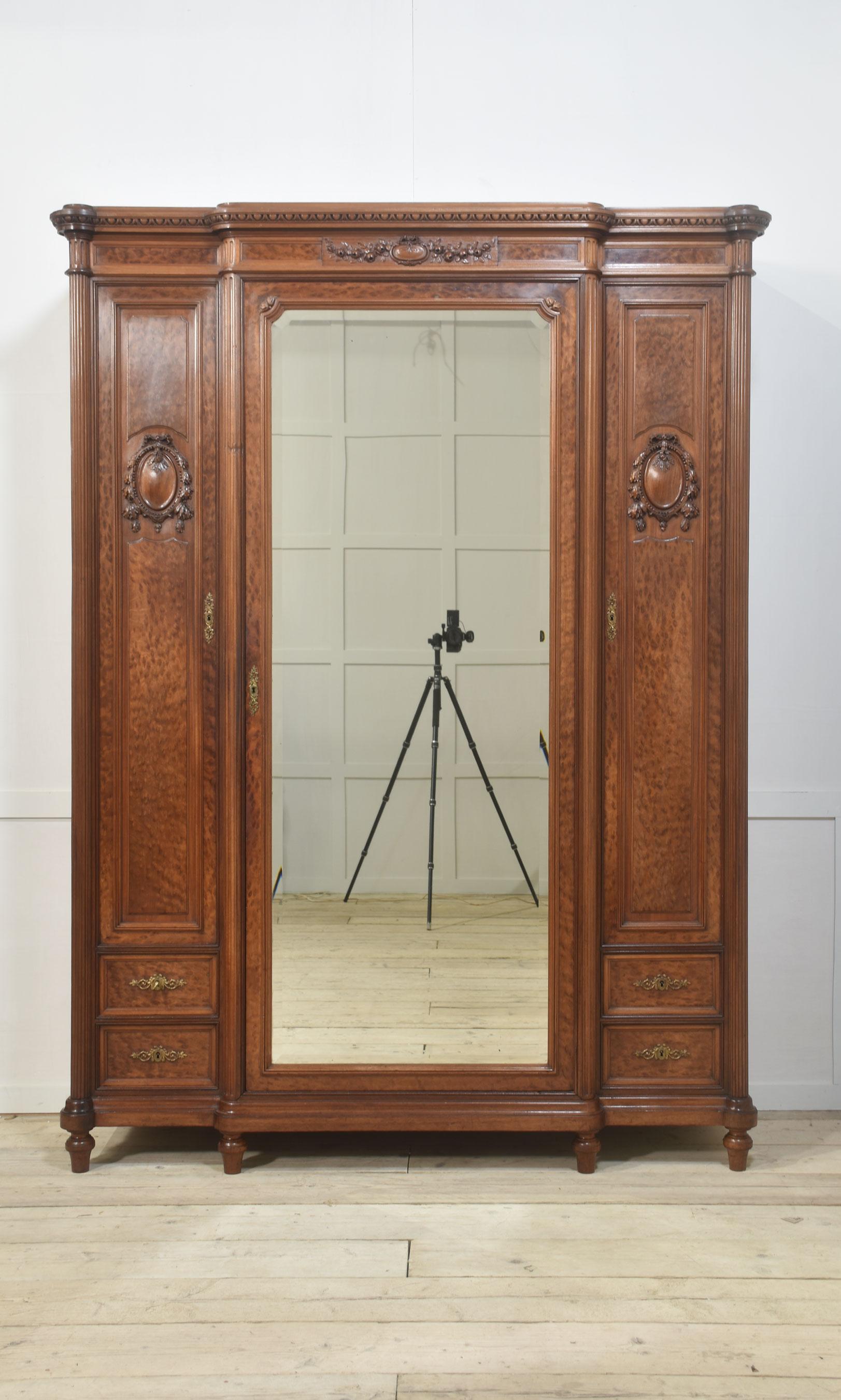 19th Century French Louis XVI Mahogany wardrobe, the breakfront top with carved detail above a large central bevelled mirror door flanked by two narrow well-figure panelled doors. Opening to reveal a large hanging area with adjustable shelving to