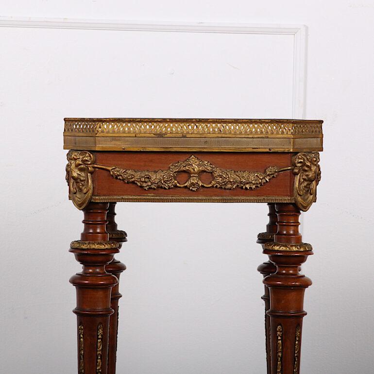 An early 20th century French Louis XVI marble top stand, the marble top with canted corners and pierced gilt gallery, the sides with ormolu swags and rams’ heads, the whole raised on four turned tapering legs with gilt mounts and joined by a gilt