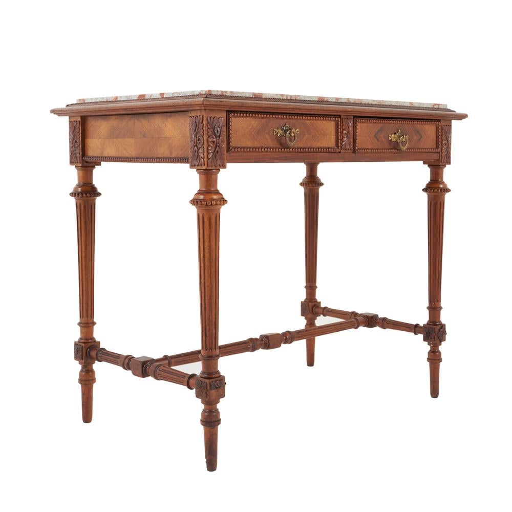 A French Louis XVI style two-drawer marble-top table or writing desk with nicely-carved details throughout, the tapering fluted legs joined by a turned stretcher.