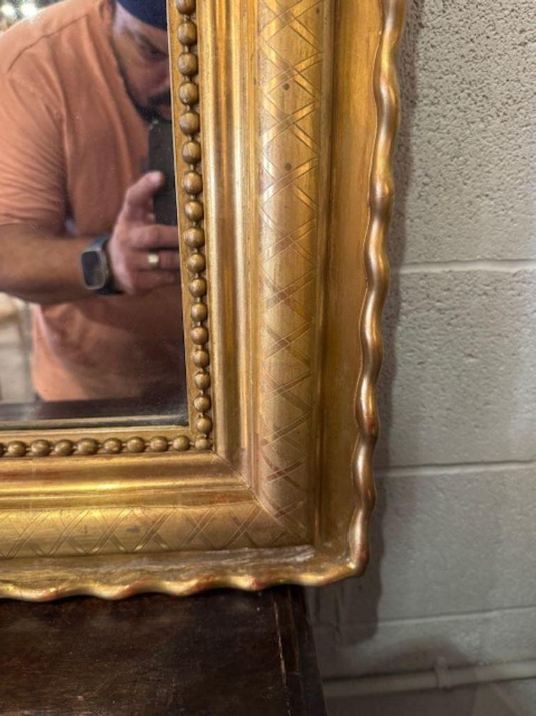 19th century French Louis XVI giltwood mirror with crest and X pattern frame. Looking to add a touch of regal elegance to your space? A French Louis XVI giltwood mirror brings neoclassical refinement with its ornate carvings, symmetrical lines, and