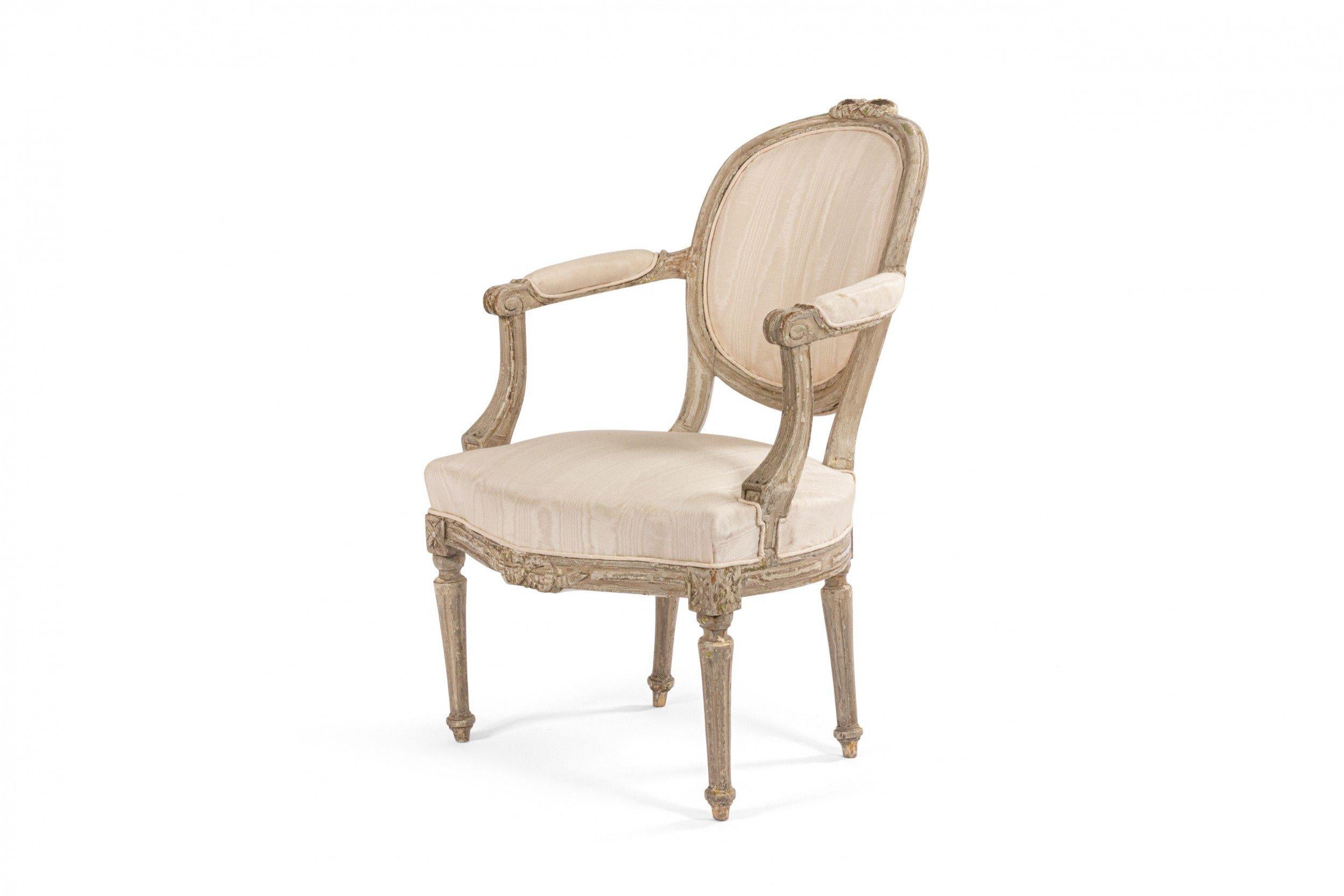 Set of 4 French Louis XVI (18th Century) white painted open arm chairs with oval back having a carved bow knot crest and a white moire upholstered seat and back.