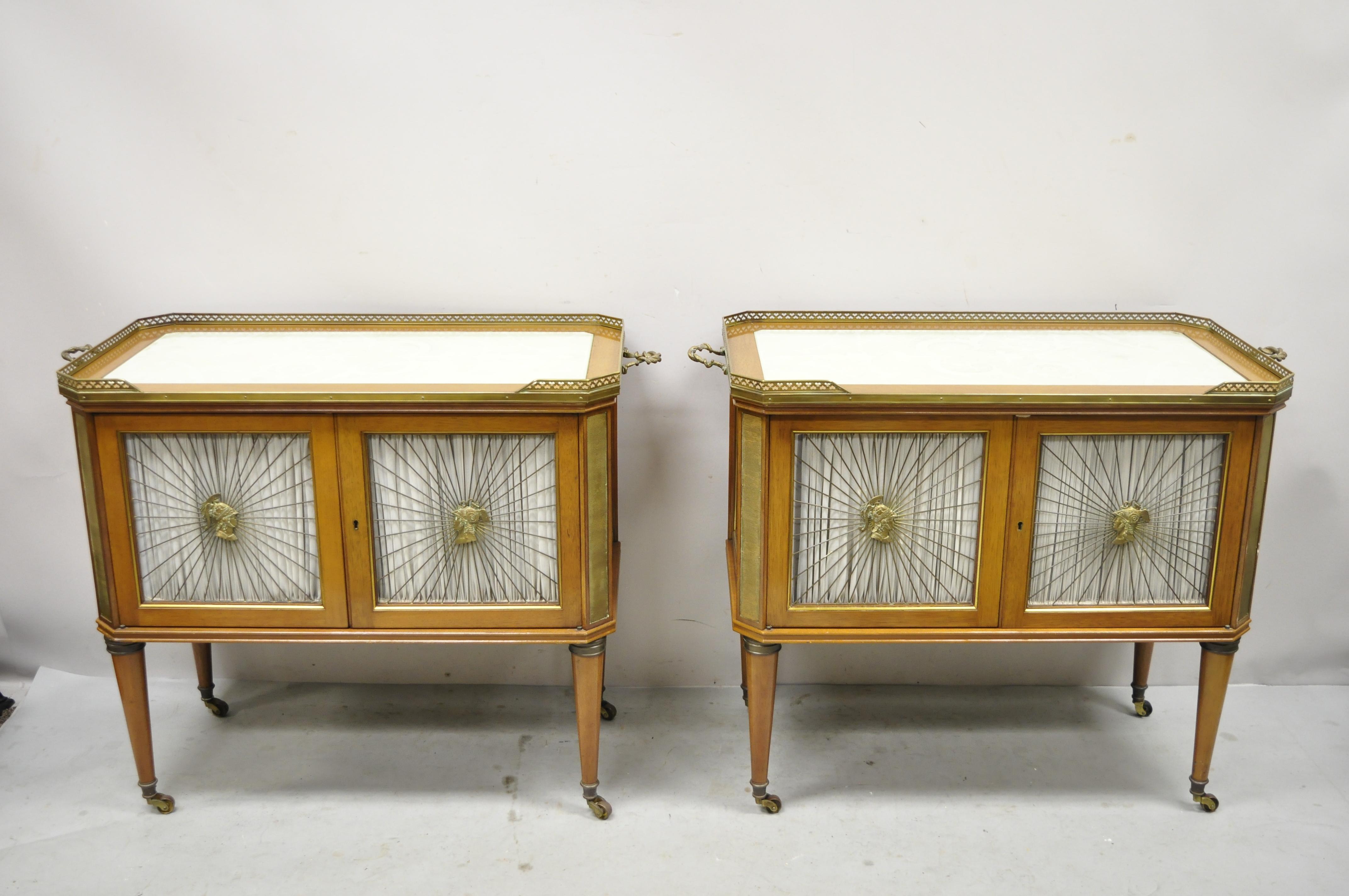 Vintage French Louis XVI neoclassical Regency style Mahogany server cabinet tables - a pair. Item features bronze mounts and gallery, soldier busts to door grills, inset glass tops, with scrollwork design, brass rolling casters, ornate side handles,