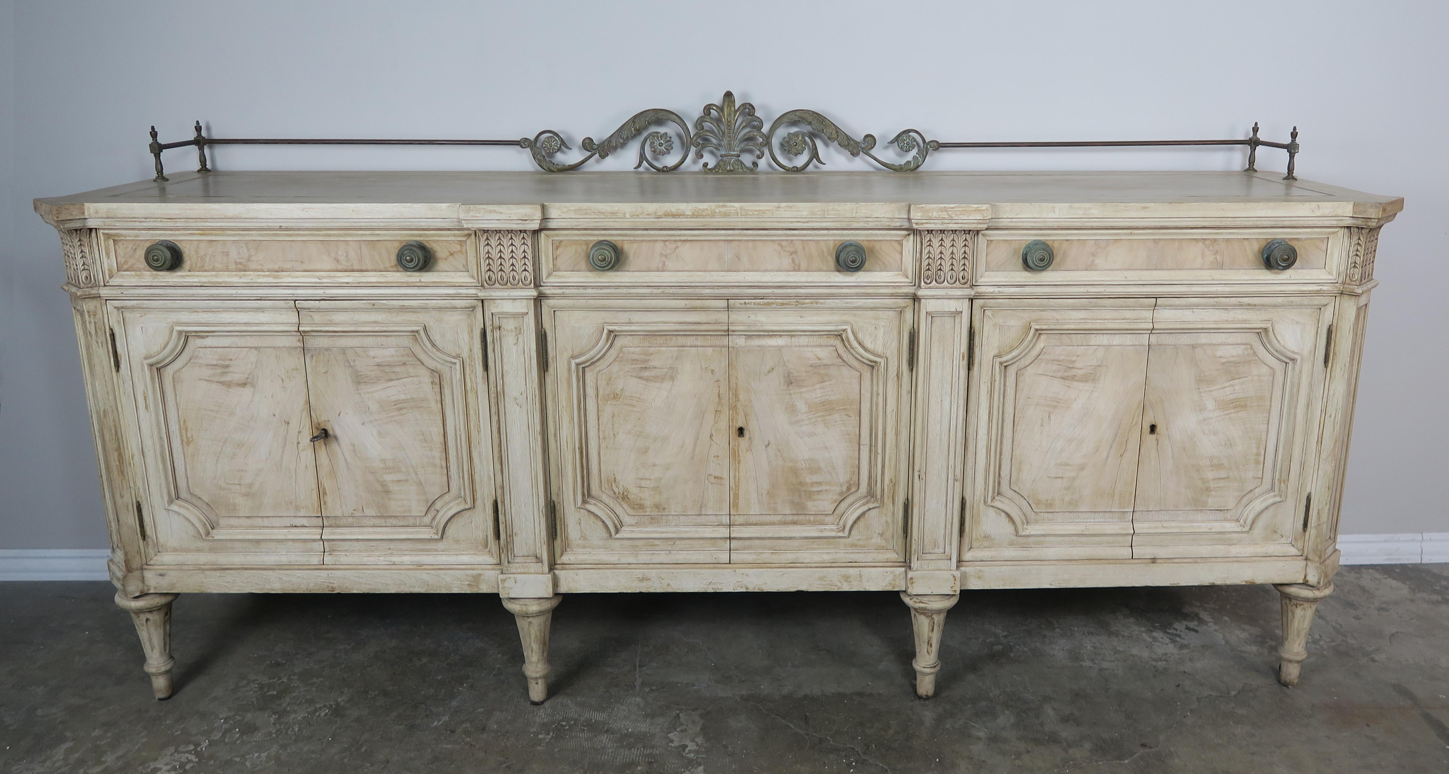 French Louis XVI bleached walnut neoclassical style sideboard with six doors and three drawer. Beautiful natural finish with a brass gallery depicting a center urn flanked by acanthus leaf detail.