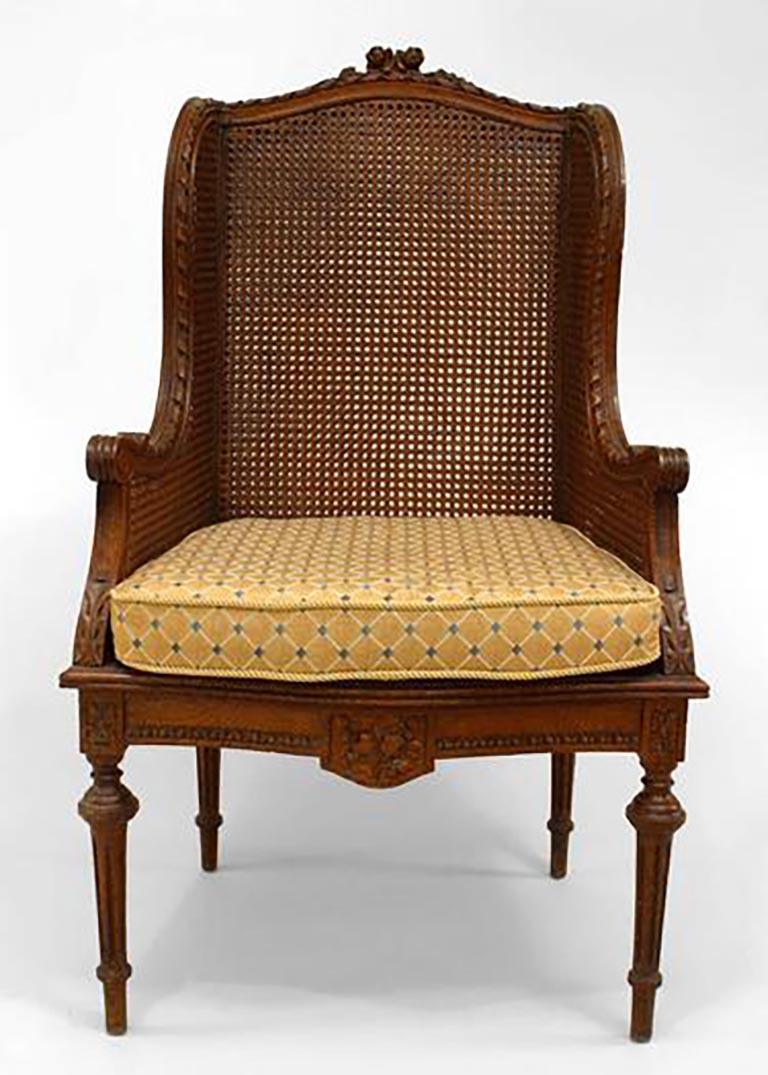 Pair of French Louis XVI style (19th century) oak wing chairs with carved frame and cane seat, back and arms with a cushion.