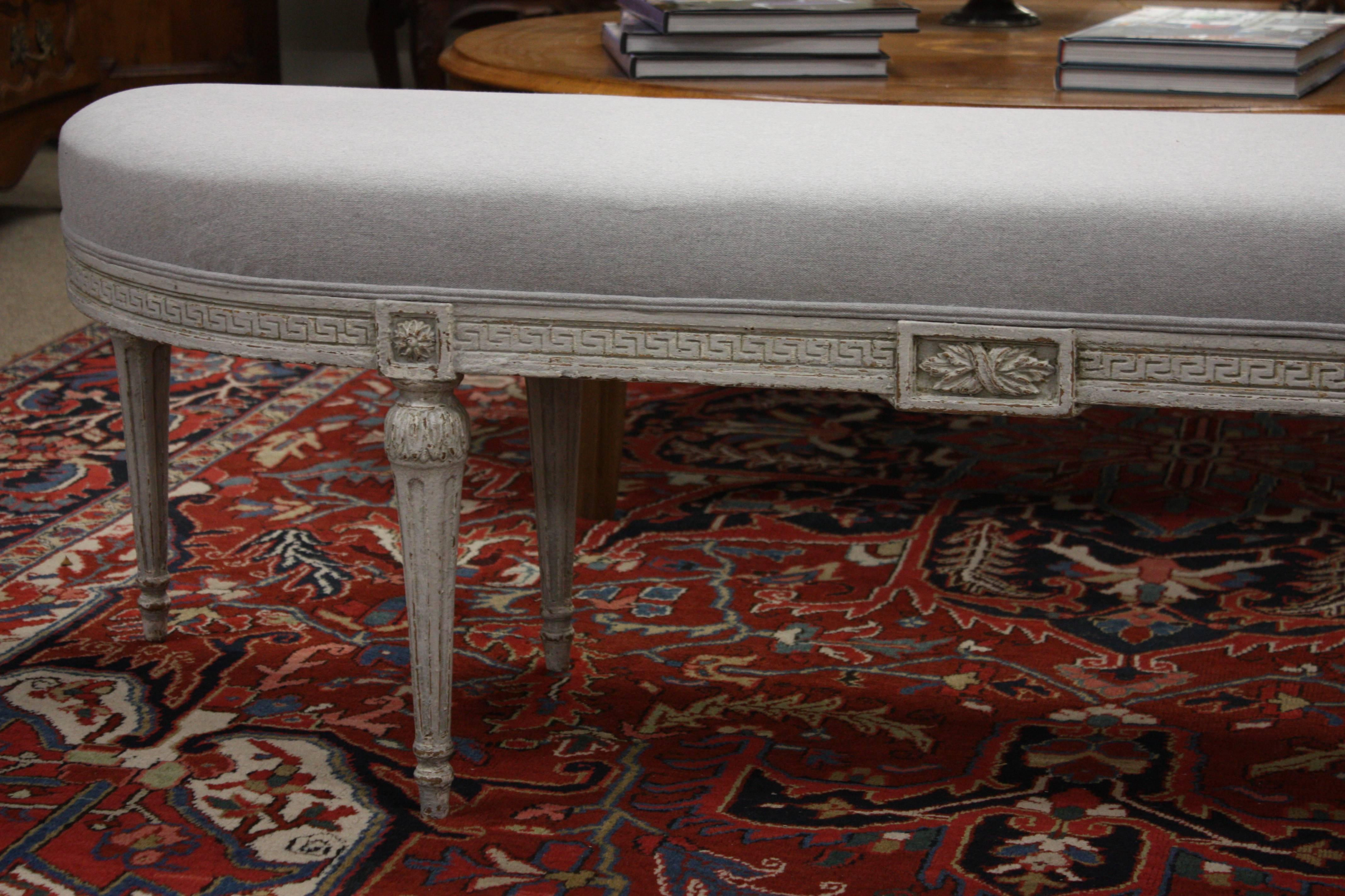 Louis XVI bench from France. Carved, circa 1910, the antique bench has six tapered legs, Greek key carvings around the apron, and is reupholstered in a neutral grey. Due to its size and narrow profile, the bench would also make the perfect piece at