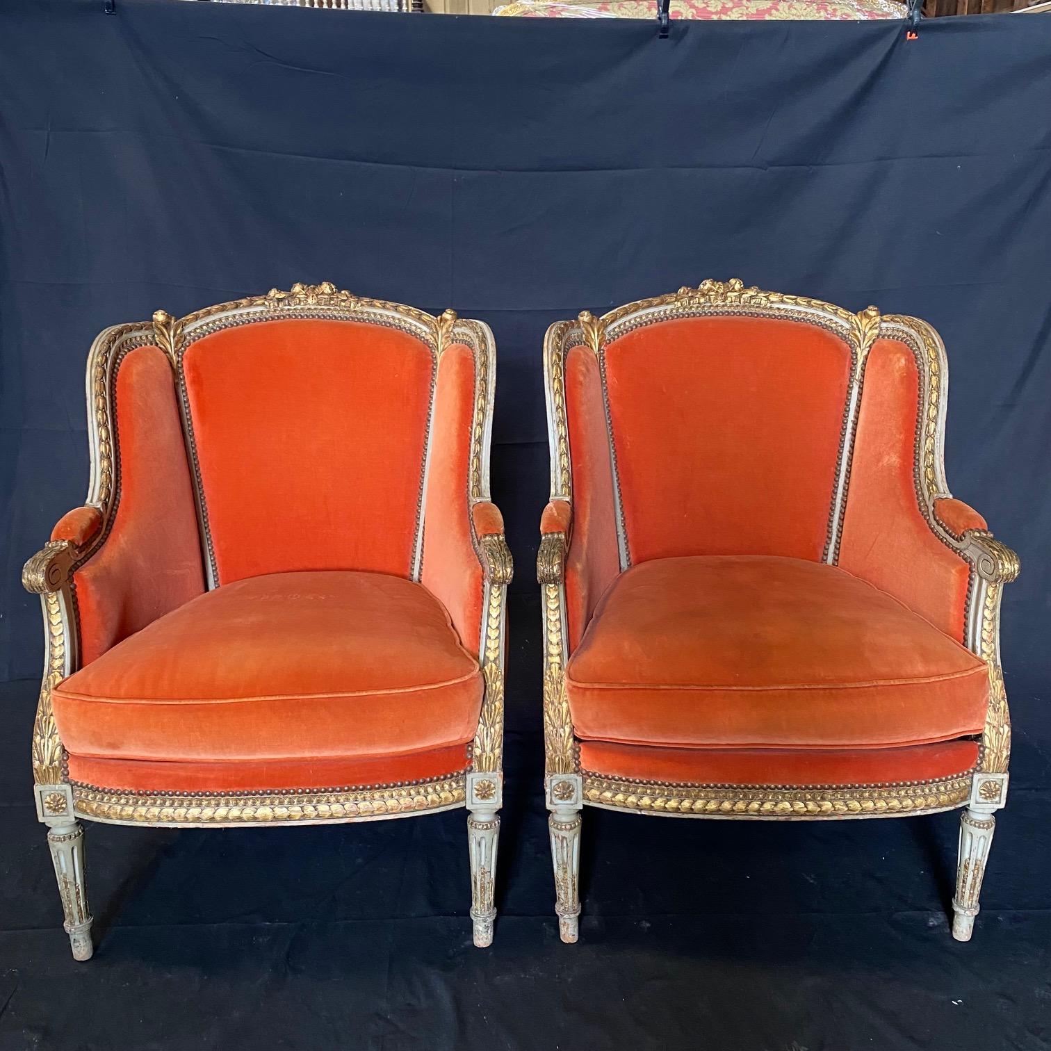 A stunning pair of antique, late 19th century French upholstered carved and gilt armchairs or wing chairs. The chairs feature carved and gilded floral swags around the back, running coin ornament along the base, carved and decorated legs and arms.