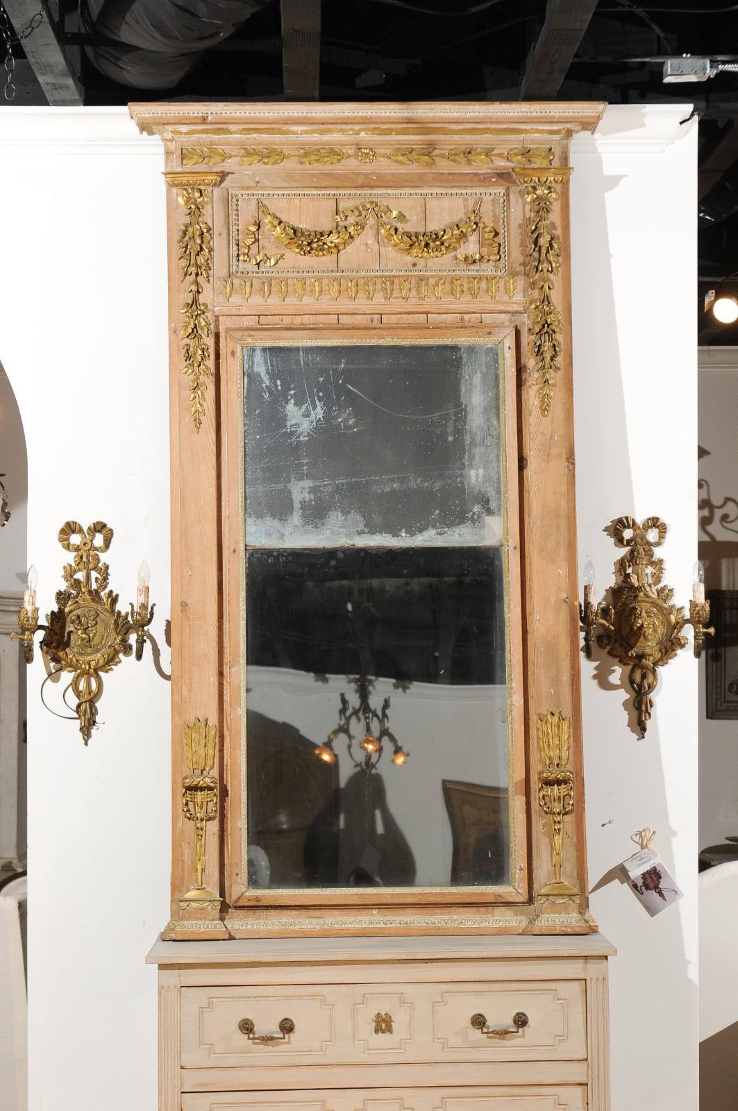 A French Louis XVI period trumeau mirror from the late 18th century, with original glass and hand carved giltwood motifs. Born in France during the reign of King Louis XVI, this trumeau mirror features a wooden frame with natural patina, accented