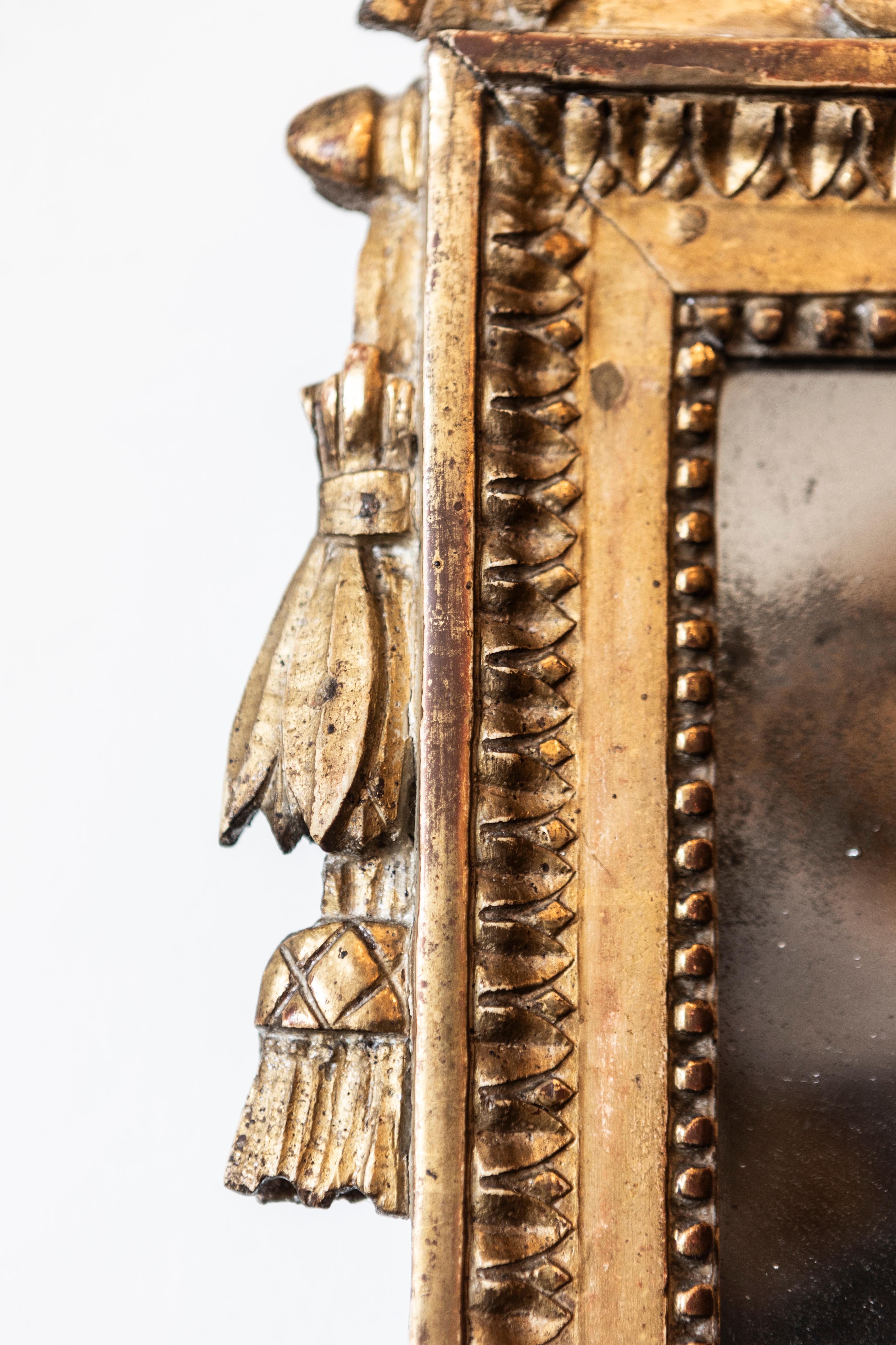Miroir en bois doré d'époque Louis XVI, vers 1790, avec une crête sculptée représentant un oiseau et des drapeaux. Ce miroir en bois doré d'époque Louis XVI, datant d'environ 1790, est un chef-d'œuvre d'artisanat et d'élégance. Le miroir présente un