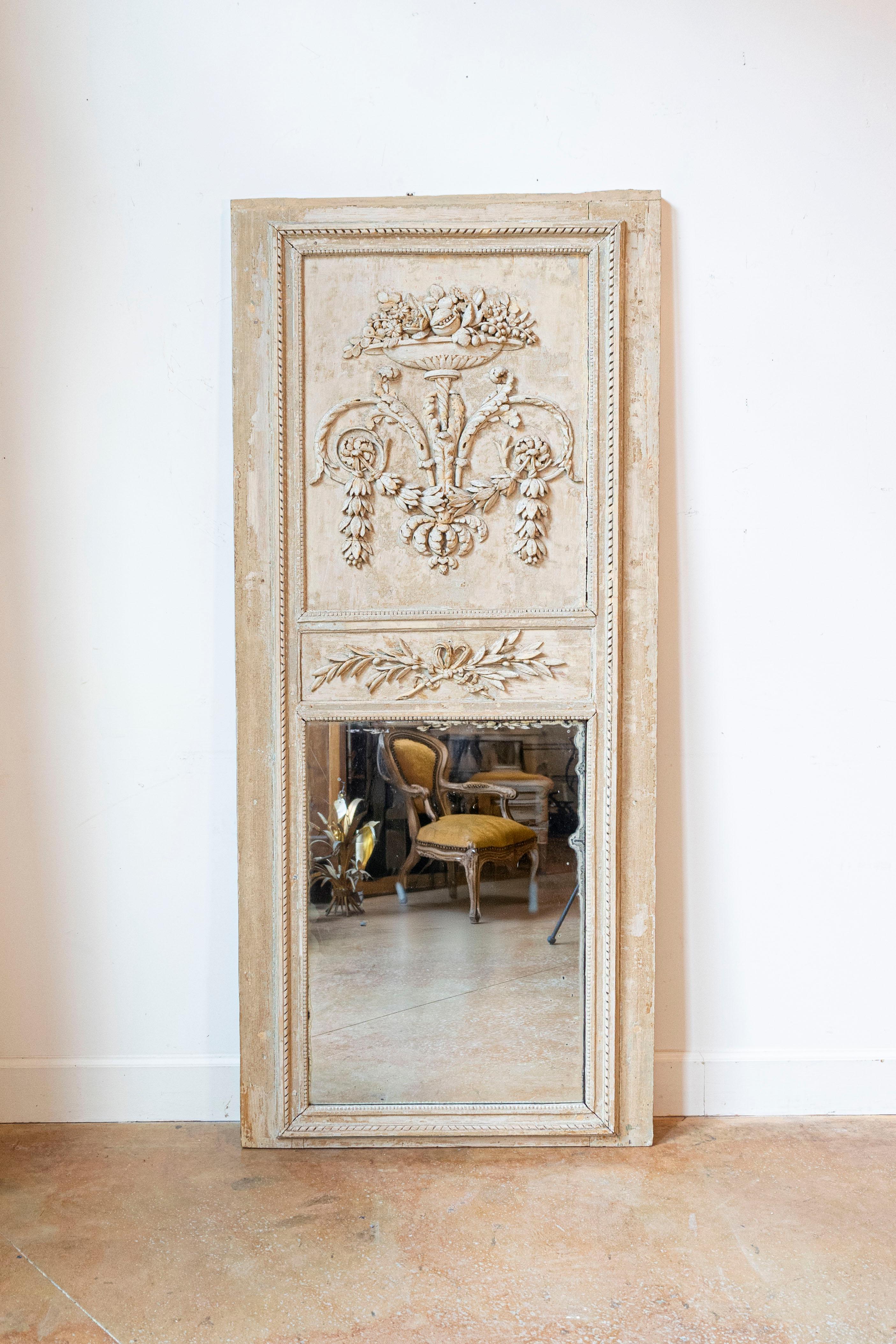 A French painted wood Louis XVI period trumeau mirror from the late 18th century, with foliage, scrollwork and urn motifs. Born in France at the end of the Age of Enlightenment, this Louis XVI trumeau mirror features a linear Silhouette, beautifully
