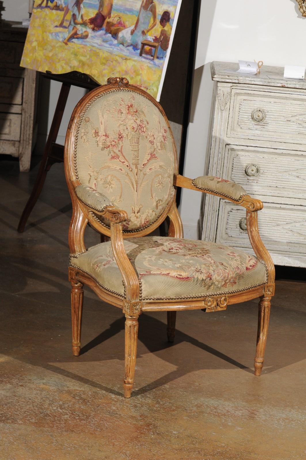 A French Louis XVI period carved wood armchair from the late 18th century with oval back and tapestry upholstery. Born during the second half of the 18th century, this exquisite single armchair features a molded oval back, adorned with carved roses