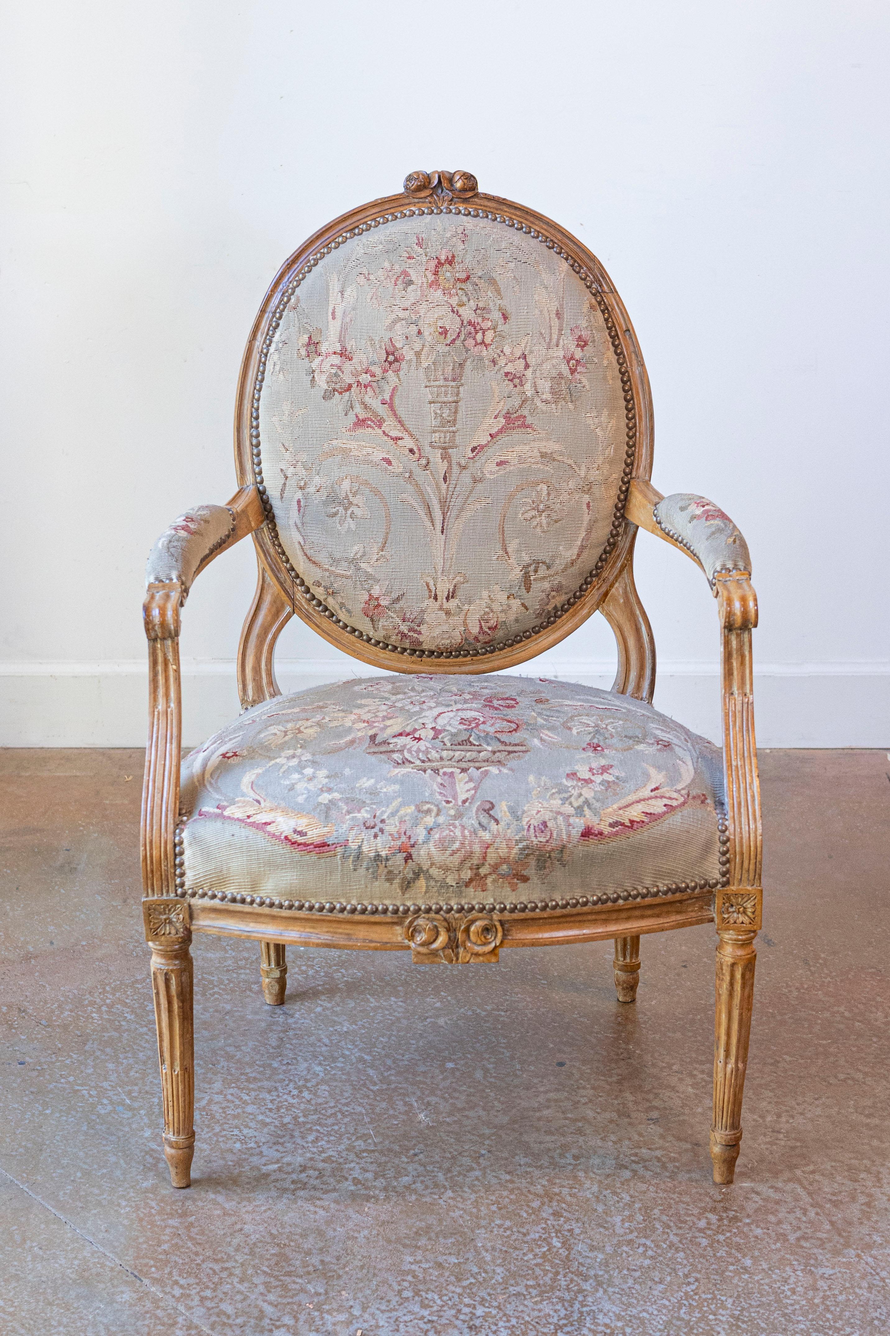 A French Louis XVI period carved wood armchair from the late 18th century with oval back and tapestry upholstery. Born during the second half of the 18th century, this exquisite single armchair features a molded oval back, adorned with carved roses