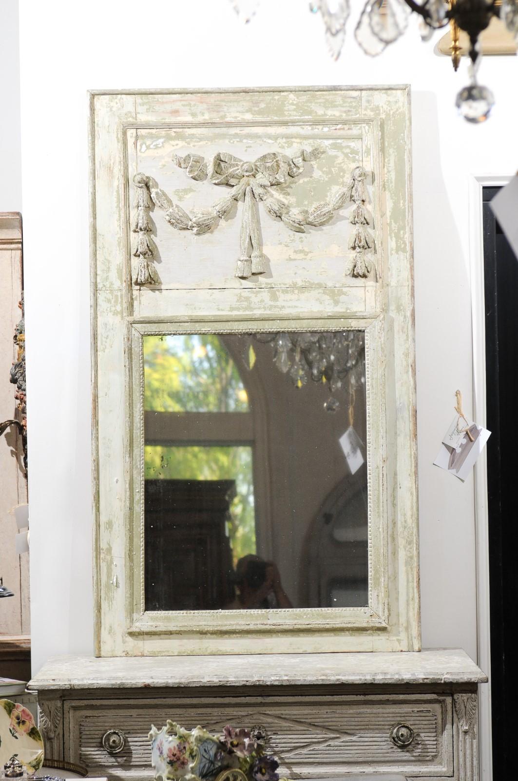 A French Louis XVI period painted wood trumeau mirror from the late 18th century, with ribbon-tied garlands and distressed finish. Born in France during the reign of King Louis XVI, this exquisite painted trumeau mirror is adorned in its upper
