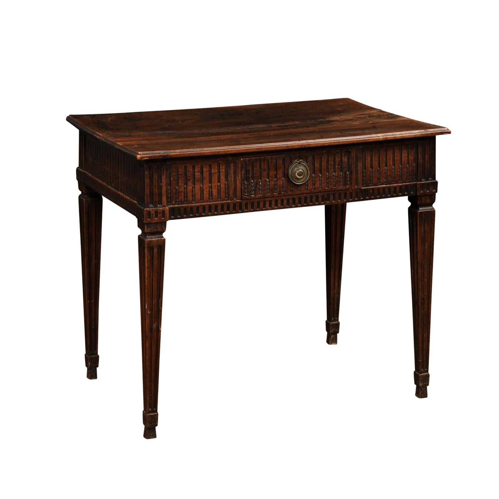 A French Louis XVI period walnut desk from the 18th century, with single drawer, carved fluted motifs, tapered legs and dark patina. Created in France during the 18th century, this walnut desk showcases the stylistic characteristics typical of the