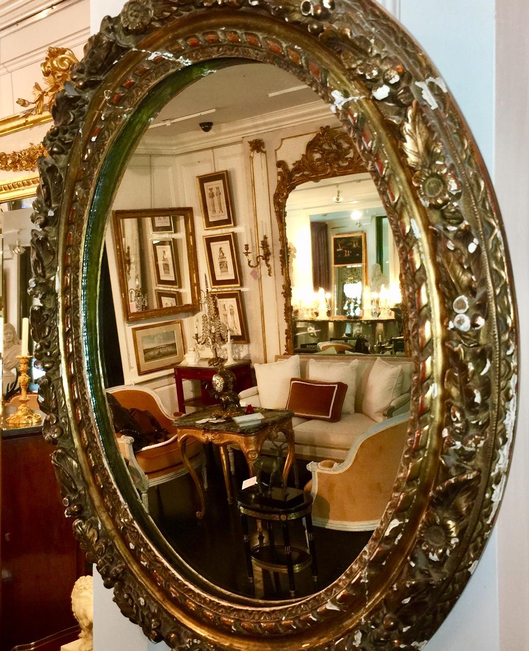 French, neoclassic style. This antique French Louis XVI period, 18th century beveled mirror features a beautifully ornate carved gilt leaf wood frame with flowers, berries and leaves. The oval frame surrounds the original beveled mirror glass which