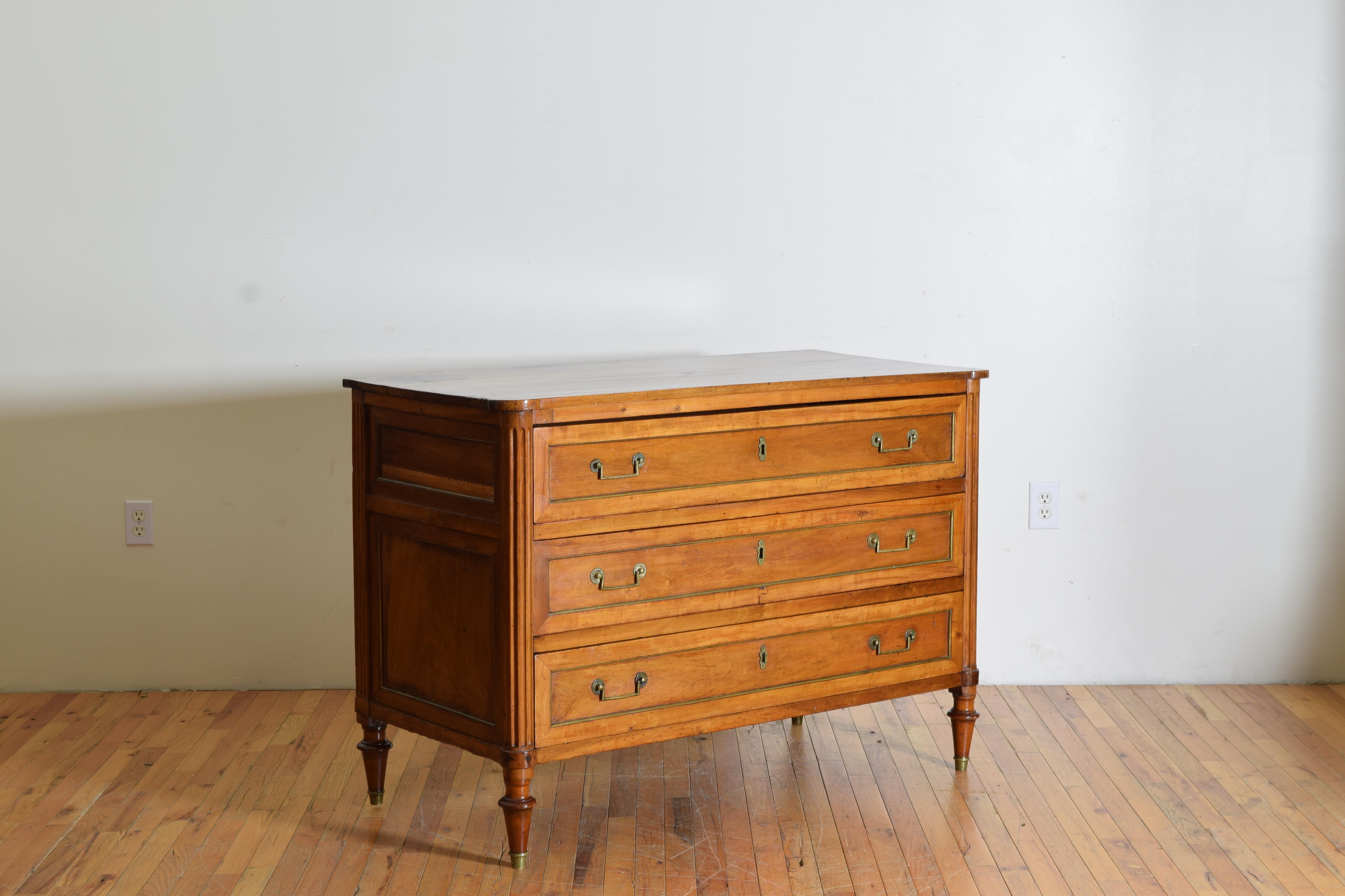 Having a rectangular top with rounded front corners above a conforming case housing three drawers trimmed in brass and retaining original brass handles, the front corners flute carved, raised on shape feet with original brass casters
