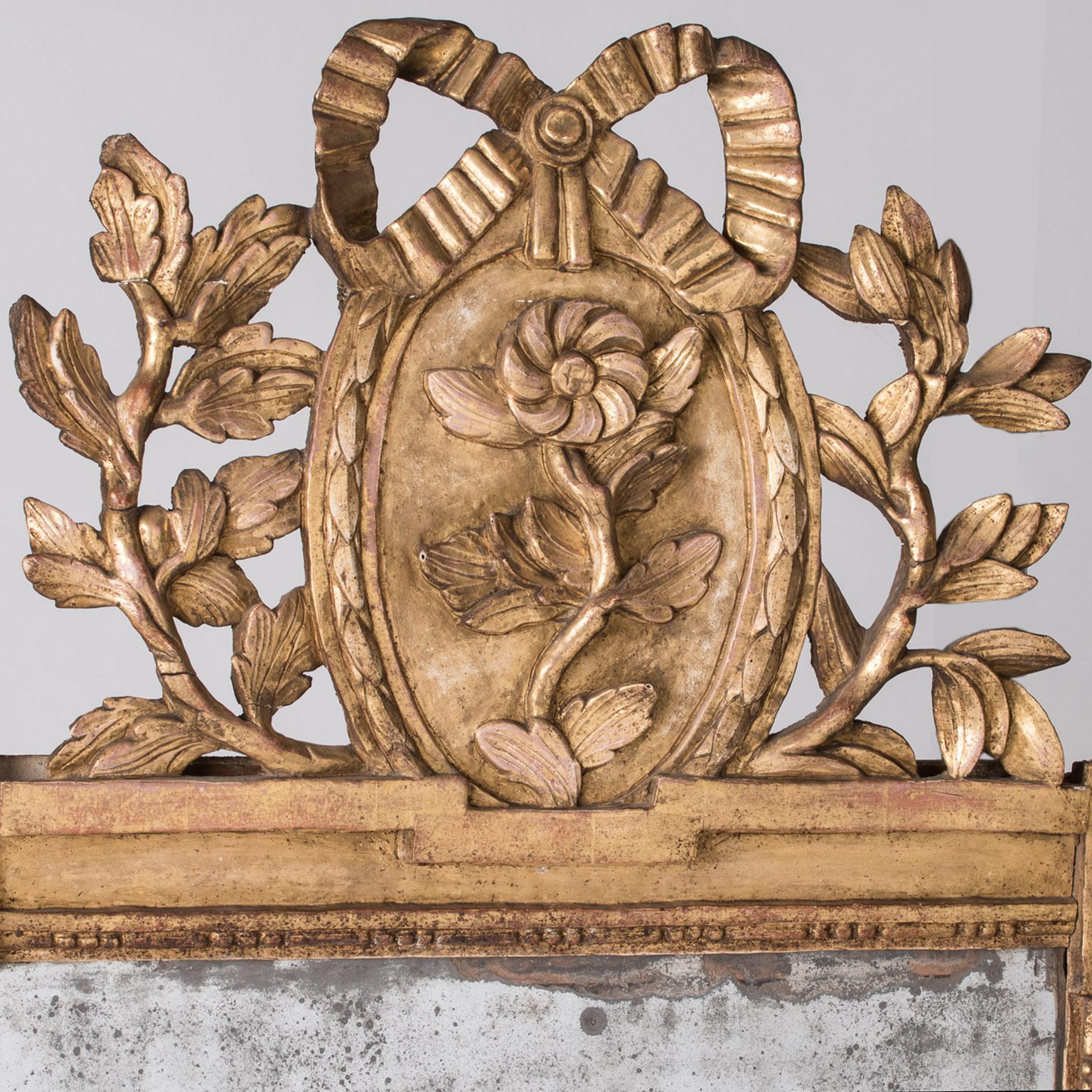 This mirror is a beauty, with original gilt throughout, and all the decorative details intact and in good condition. The top is adorned with a masterful bow over an oval medallion, framing a flower surrounded by leaves and vines. The divided