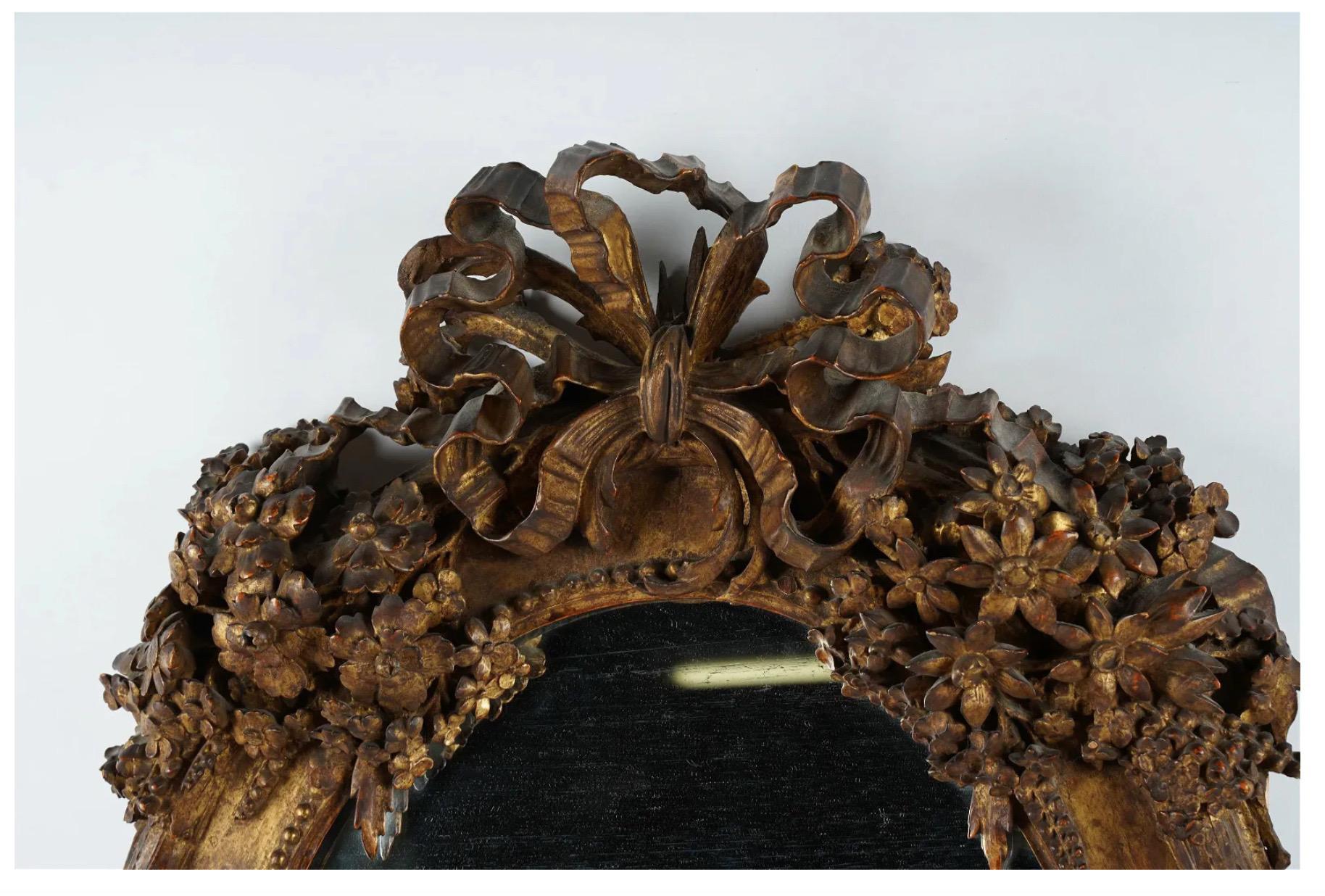 This is one of the most stunning and unique period Louis XVI mirrors we have seen. The depth and finely detailed floral carvings include sunflowers, lilies, daisies and roses. The bows at both the top and bottom of the mirror are elaborate and