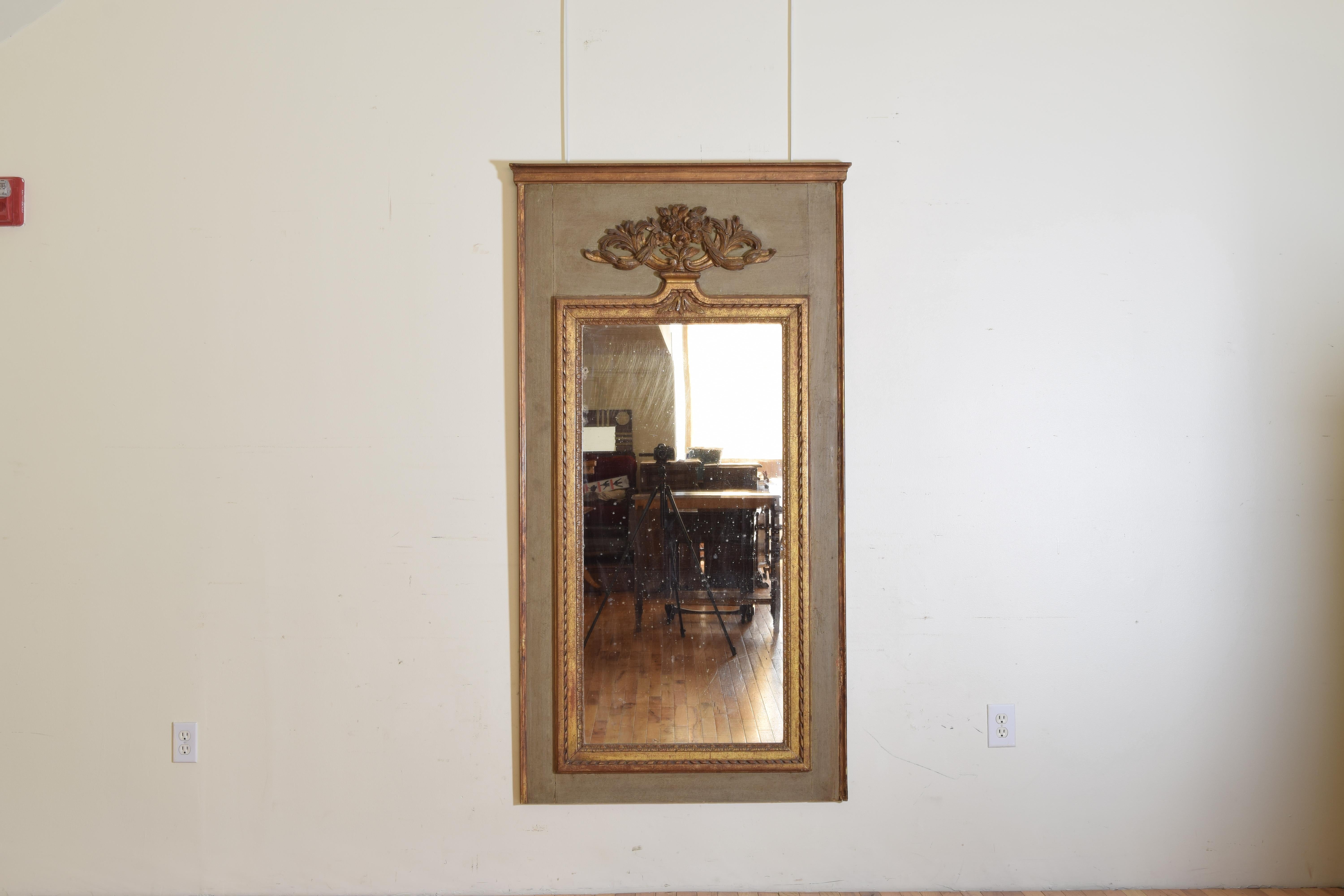 Of rectangular vertical form this mirror has a painted ground with carved giltwood crown and side moldings, the inner section with ribbon carved moldings and an urn shaped upper section issuing leaf forms and floral sprays.