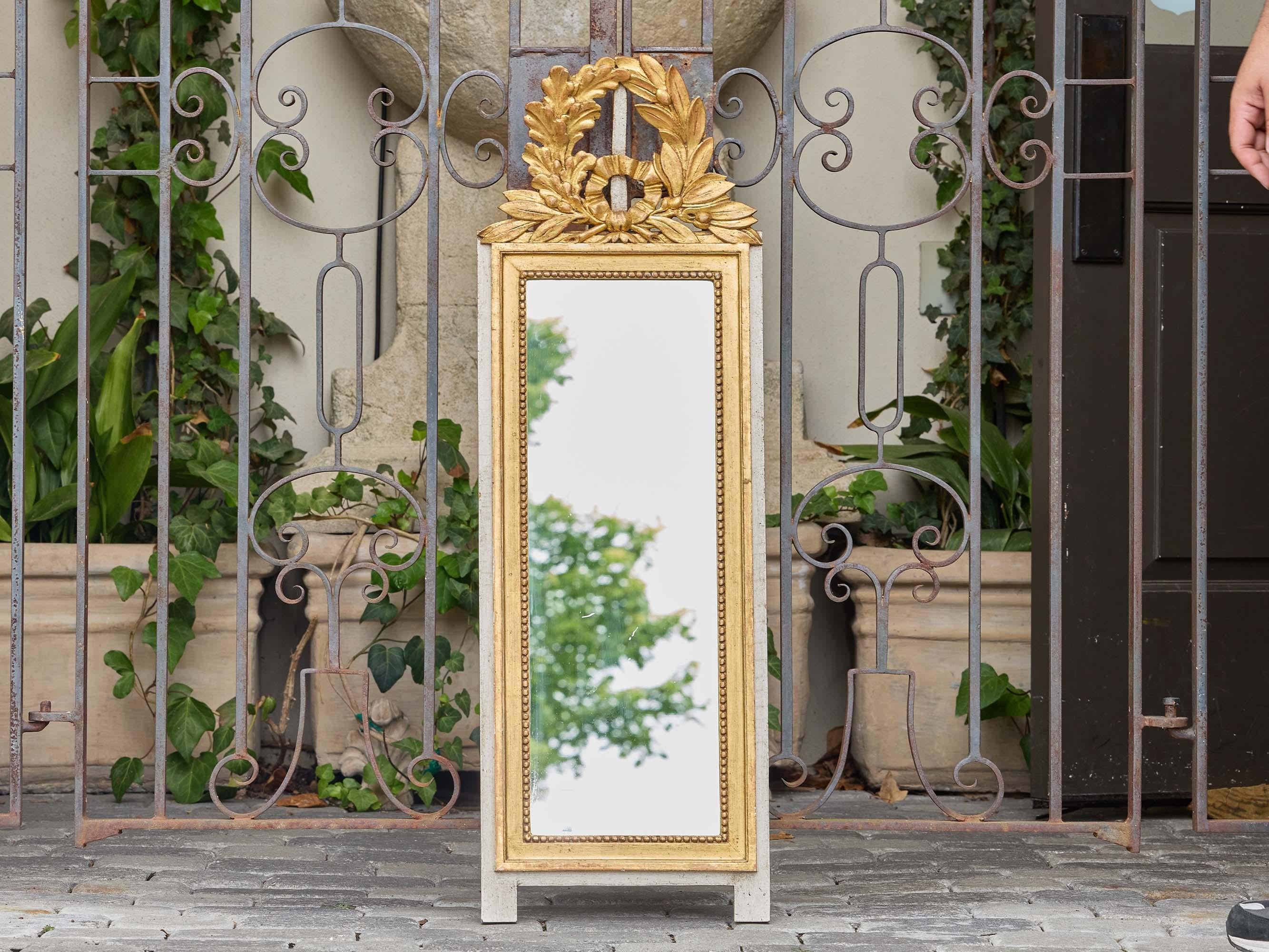 Questo specchio francese in legno dorato in stile Luigi XVI, risalente al 1920 circa, presenta un'estetica raffinata e neoclassica, ancorata da una silhouette alta e stretta ideale per l'accento architettonico. La cornice è intagliata in un profilo