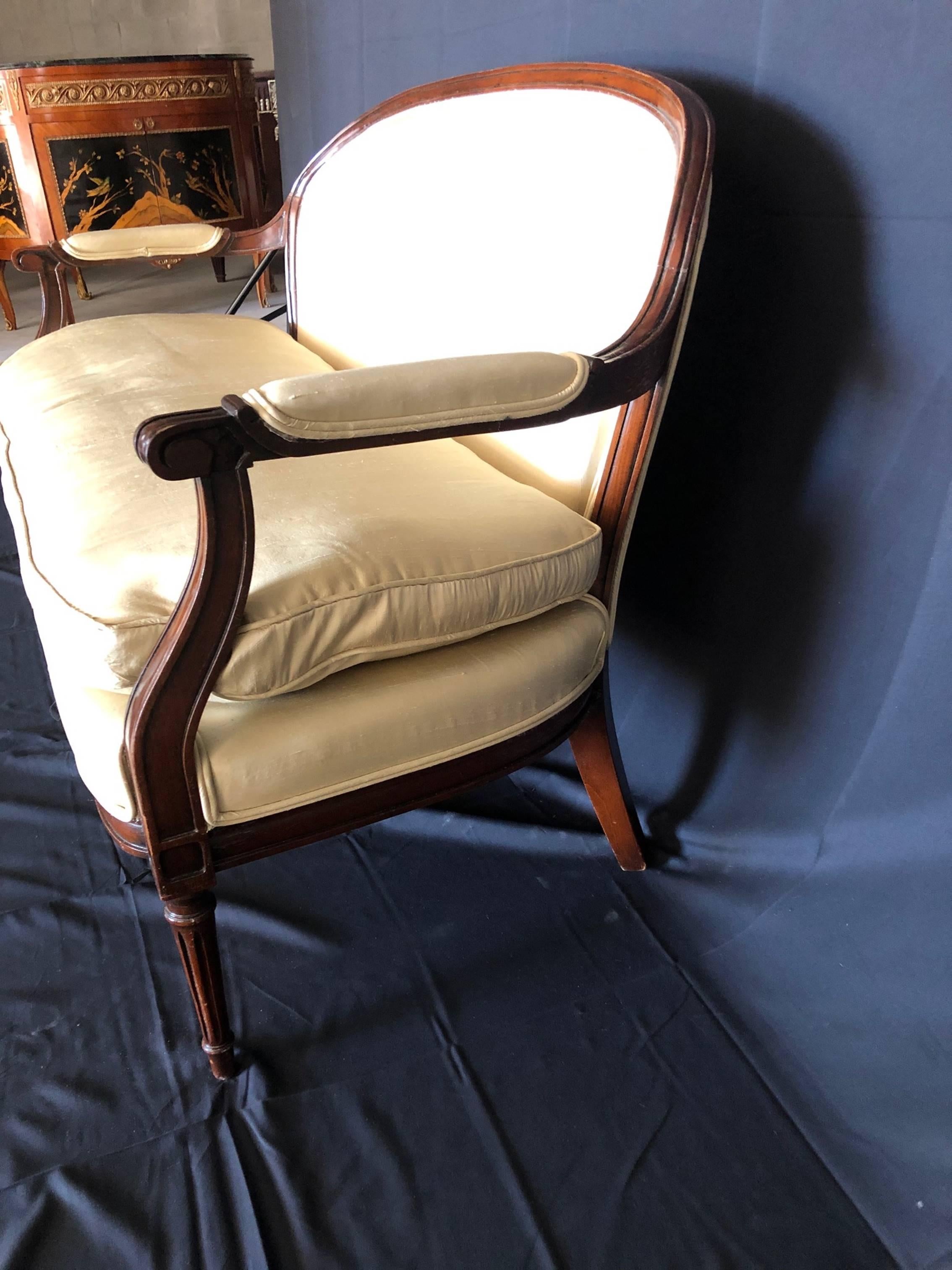 Beautiful Louis XVI style mahogany loveseat or settee with sumptuous high quality ivory silk and down seat cushion and upholstered arm rests. Silk has a few minor marks; see photos. Nicely carved details and tapered elegant legs. #2295.