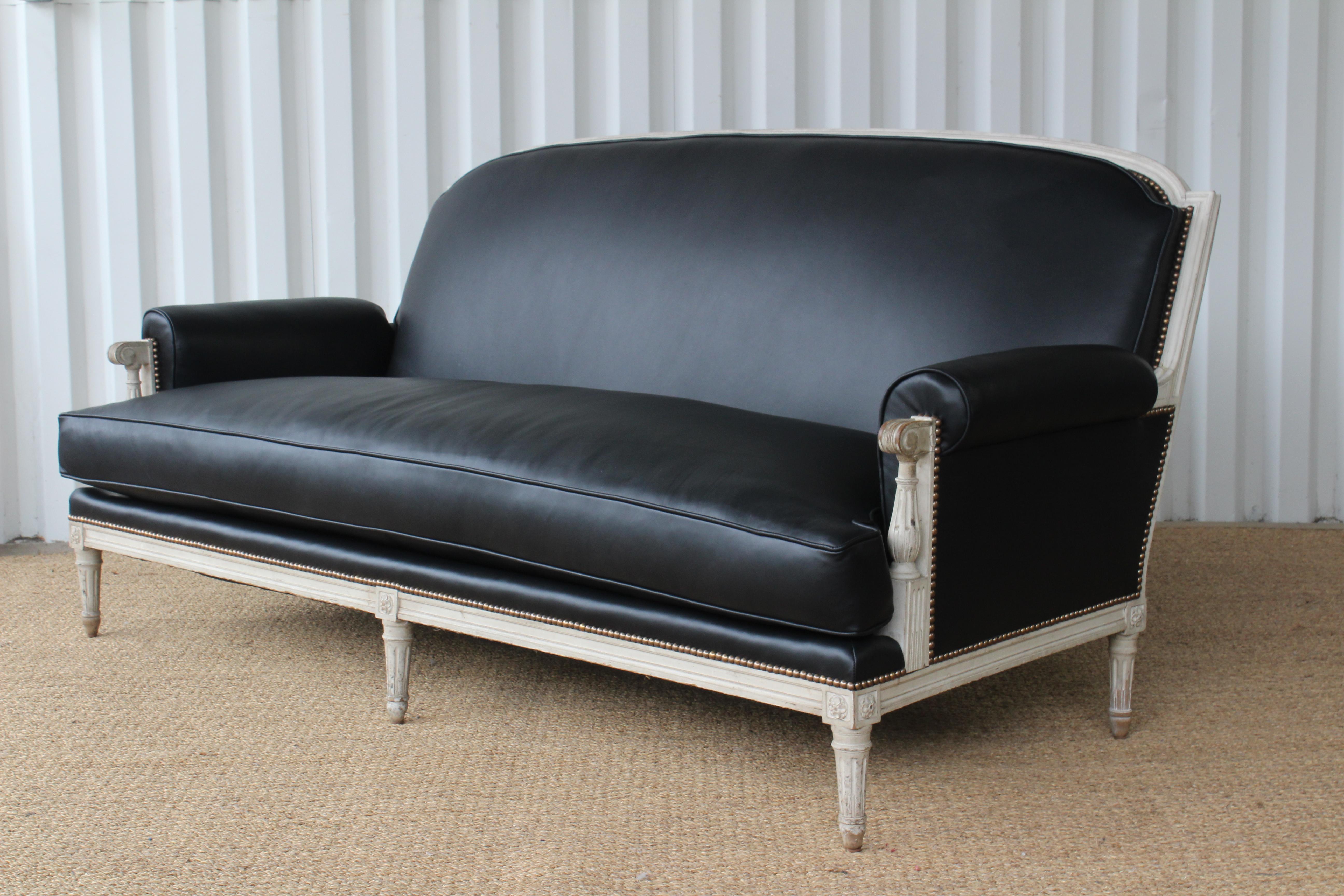 Antique Louis XVI sofa. This sofa has been reupholstered in a soft black genuine leather with antique brass nailhead detailing. The painted frame is in original condition with a wonderful patina. New springs, foam, and down filled seat