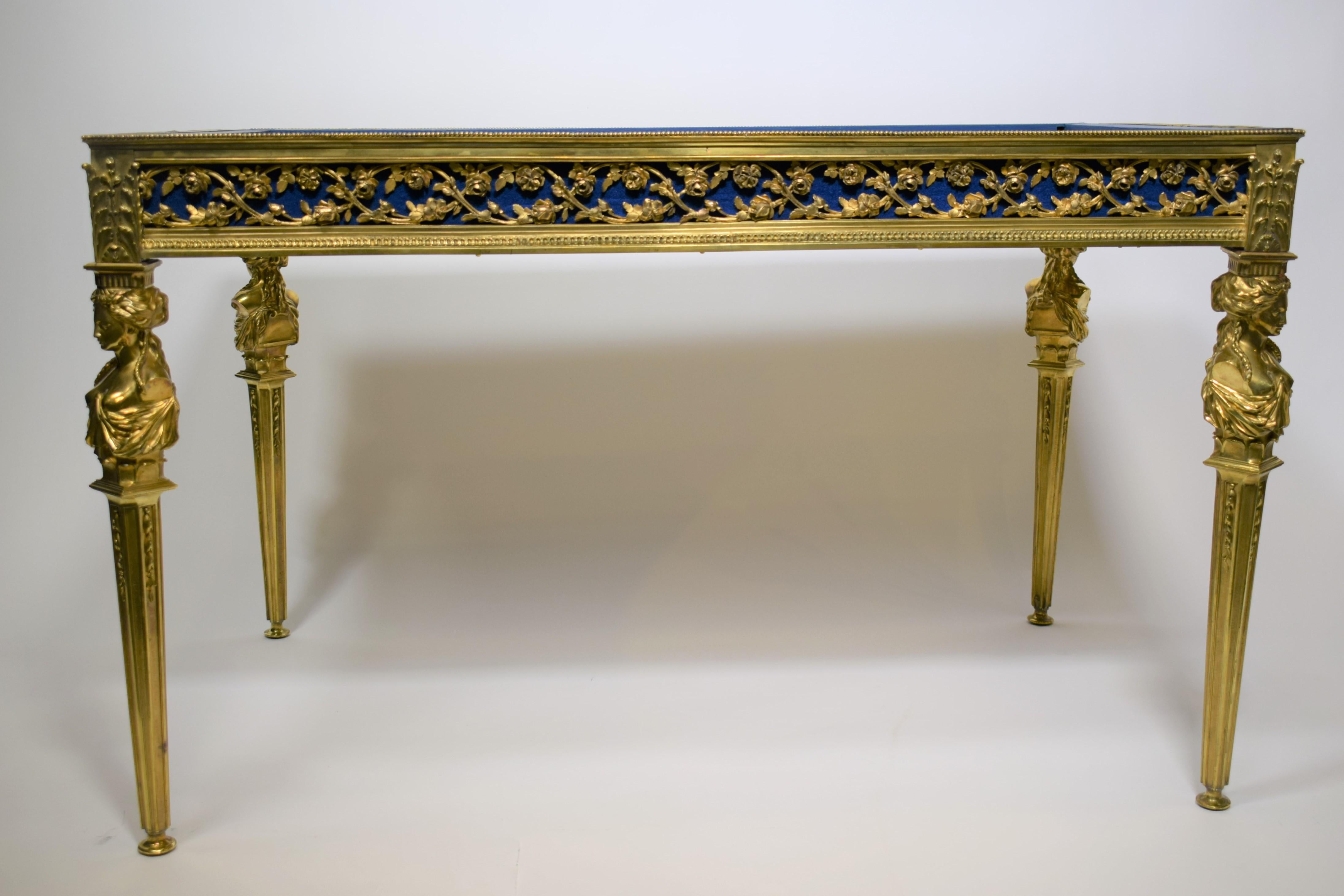 French, 19th century. Cast bronze and glazed vitrine table in the Louis XVI neoclassical taste, having a hinged crystal beveled top with rais-de-coeur edge, open scrolled foliate sides, and rising on tapering draped caryatid-form legs, in the manner