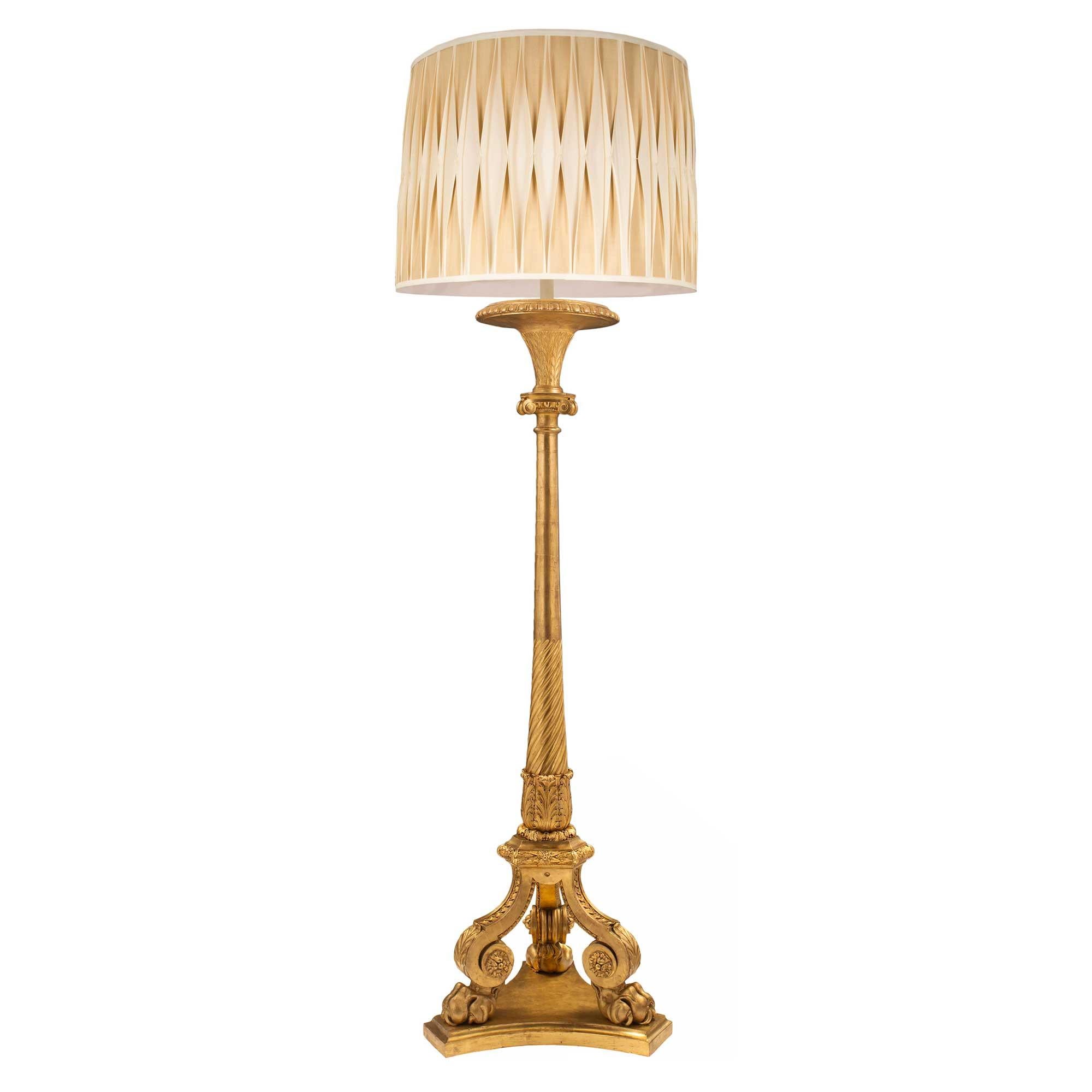 Un élégant lampadaire en bois doré de grande taille, de style Louis XVI, datant du milieu du XIXe siècle. La lampe est surélevée par une base triangulaire mouchetée aux côtés concaves au-dessus de supports demi-ronds. Au-dessus se trouvent