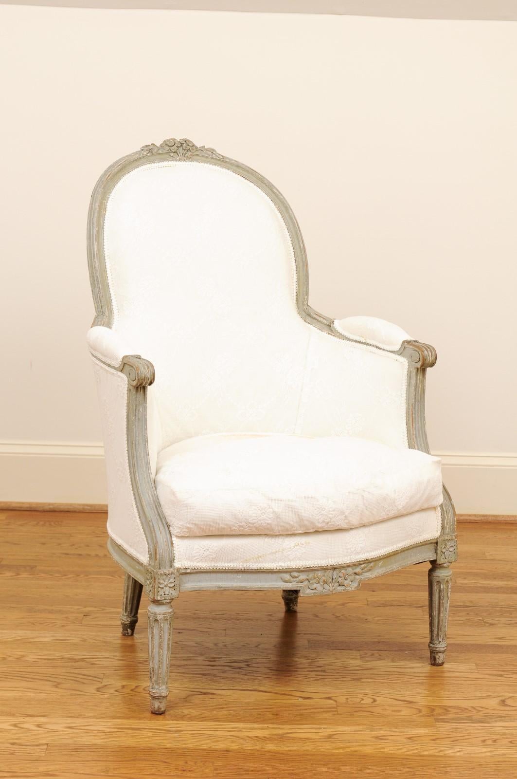 A French Louis XVI style painted wood bergère chair from the mid-19th century, with carved floral decor and new upholstery. Created in France during the second quarter of the 19th century, this bergère chair features a slightly slanted back, adorned