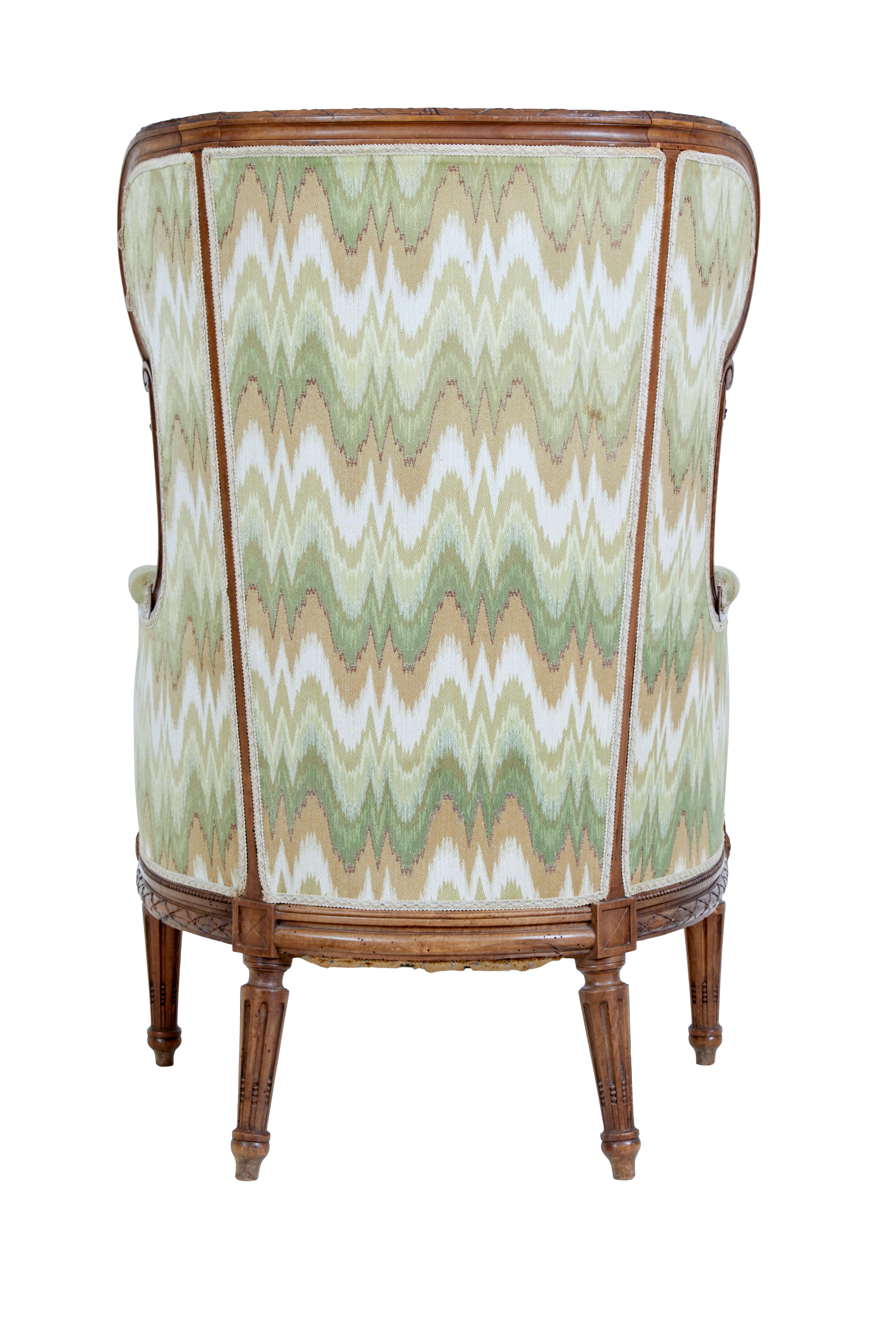 A French Louis XVI style walnut bergère à oreilles circa 1870 with carved décor and fluted legs. Transport yourself to the charm of 19th-century French décor with this Louis XVI style walnut wingback bergère chair, circa 1870. The hue of walnut and