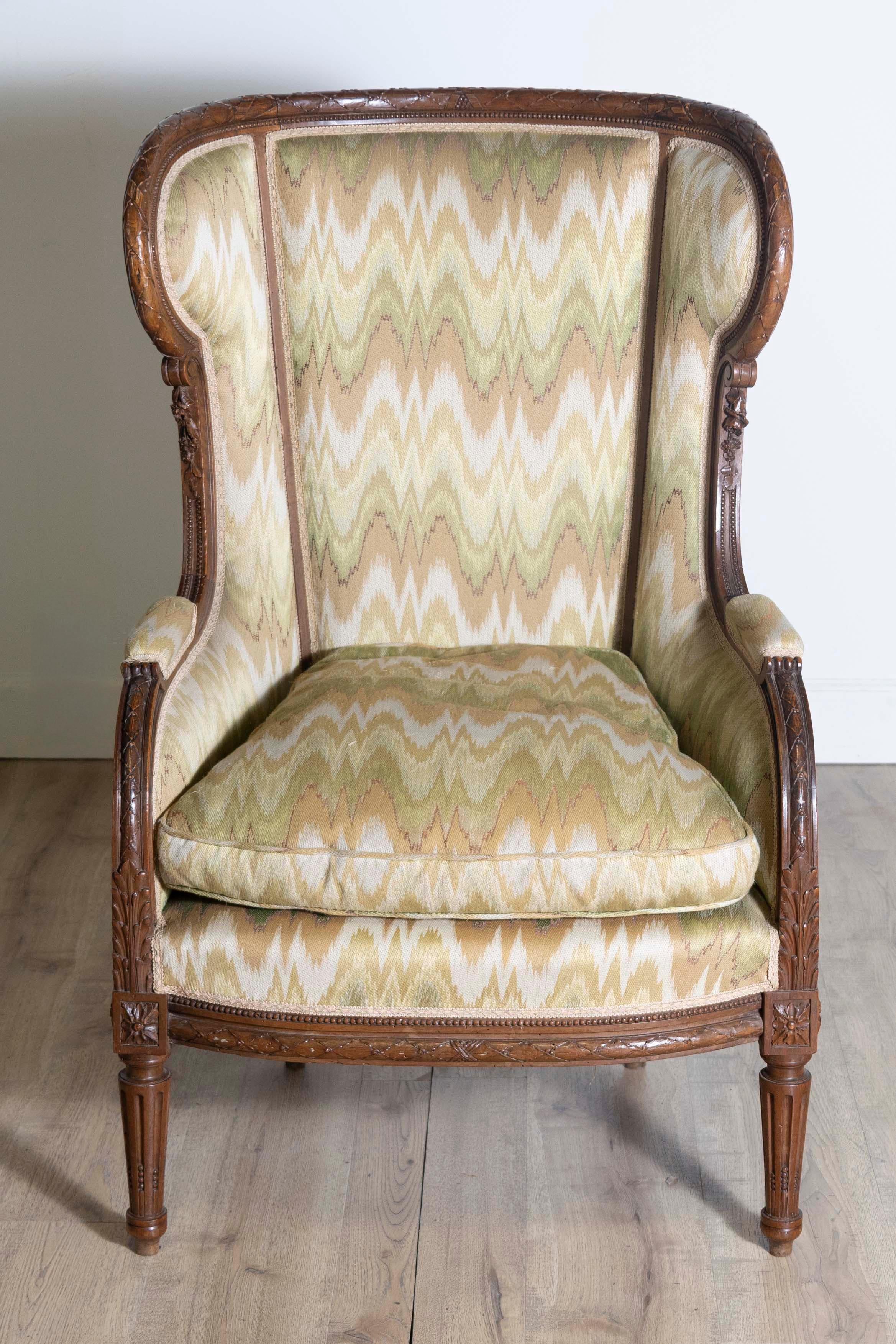 Bergère à oreilles en noyer de style Louis XVI, vers 1870, avec décor sculpté et pieds cannelés. Transportez-vous dans le charme de la décoration française du XIXe siècle avec cette chaise bergère à oreilles en noyer de style Louis XVI, vers 1870.