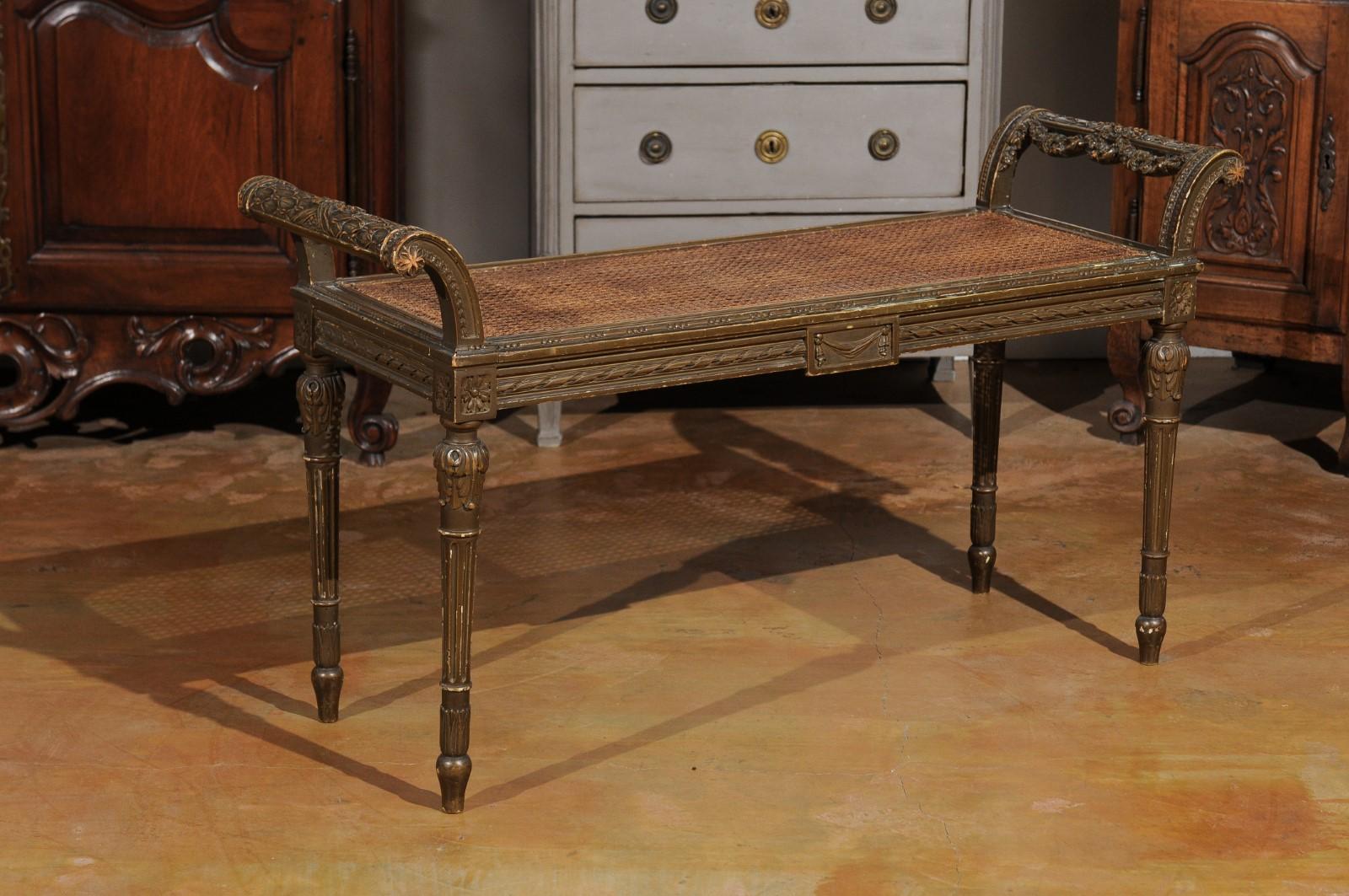 A French Louis XVI style carved wooden bench from the late 19th century, with cane seat and fluted legs. Born in France during the last quarter of the 19th century, this exquisite Louis XVI style bench features a rectangular cane seat flanked