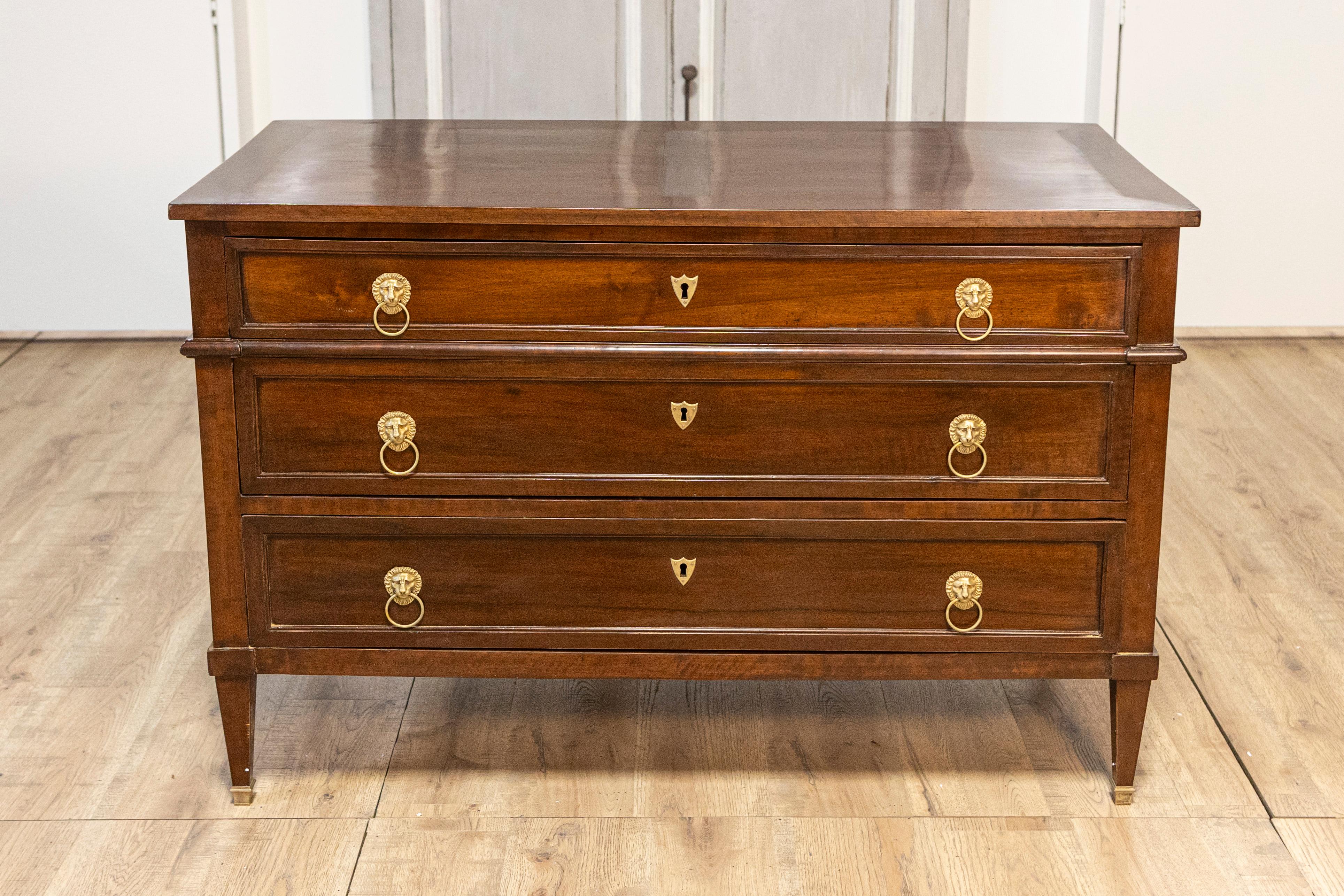 A French Louis XVI style walnut commode from circa 1890 with three drawers and brass lion head hardware. This splendid French Louis XVI style walnut commode, dating back to circa 1890, merges classic design with functional elegance. It boasts three