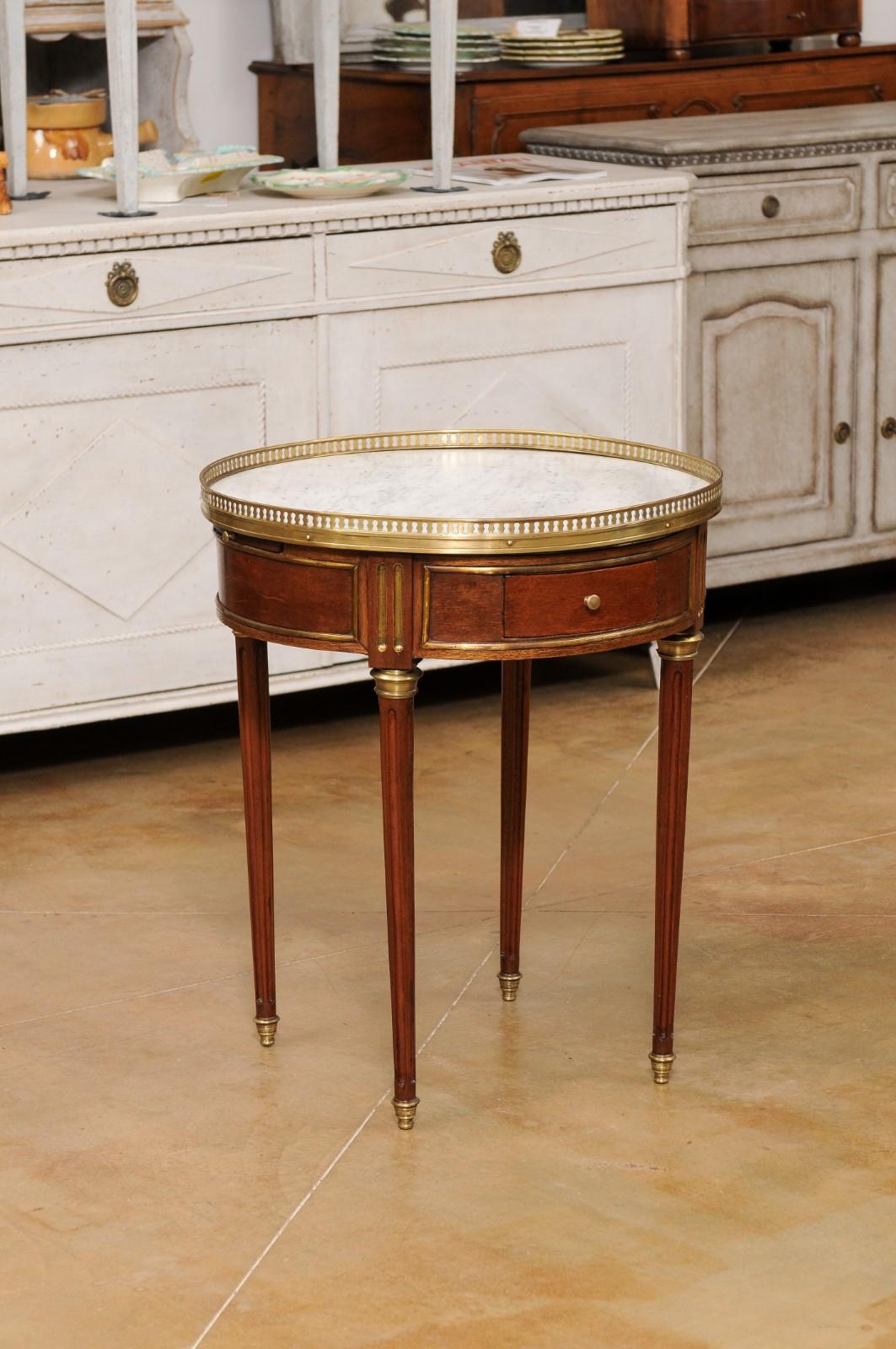A French Louis XVI style bouillotte table from the 19th century with white marble top, brass gallery, drawers and fluted legs. Created in France during the last decade of the 19th century, this elegant bouillotte table features a white veined marble