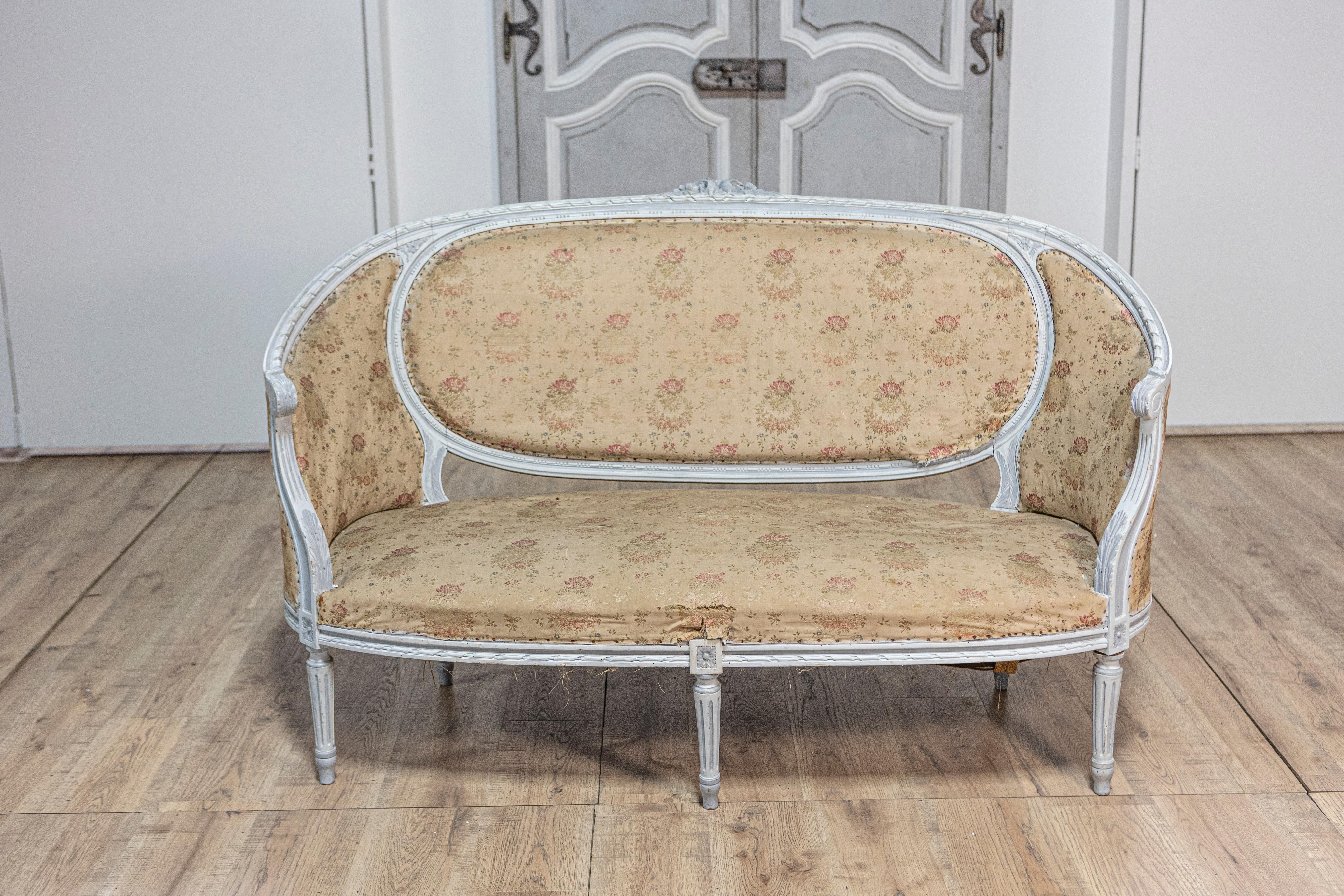 A French Louis XVI style sofa from circa 1900 with soft light blue painted finish, carved floral motif on the crest, scrolling arms and fluted legs. This French Louis XVI style sofa, known as a Canapé corbeille, hails from circa 1900 and boasts a