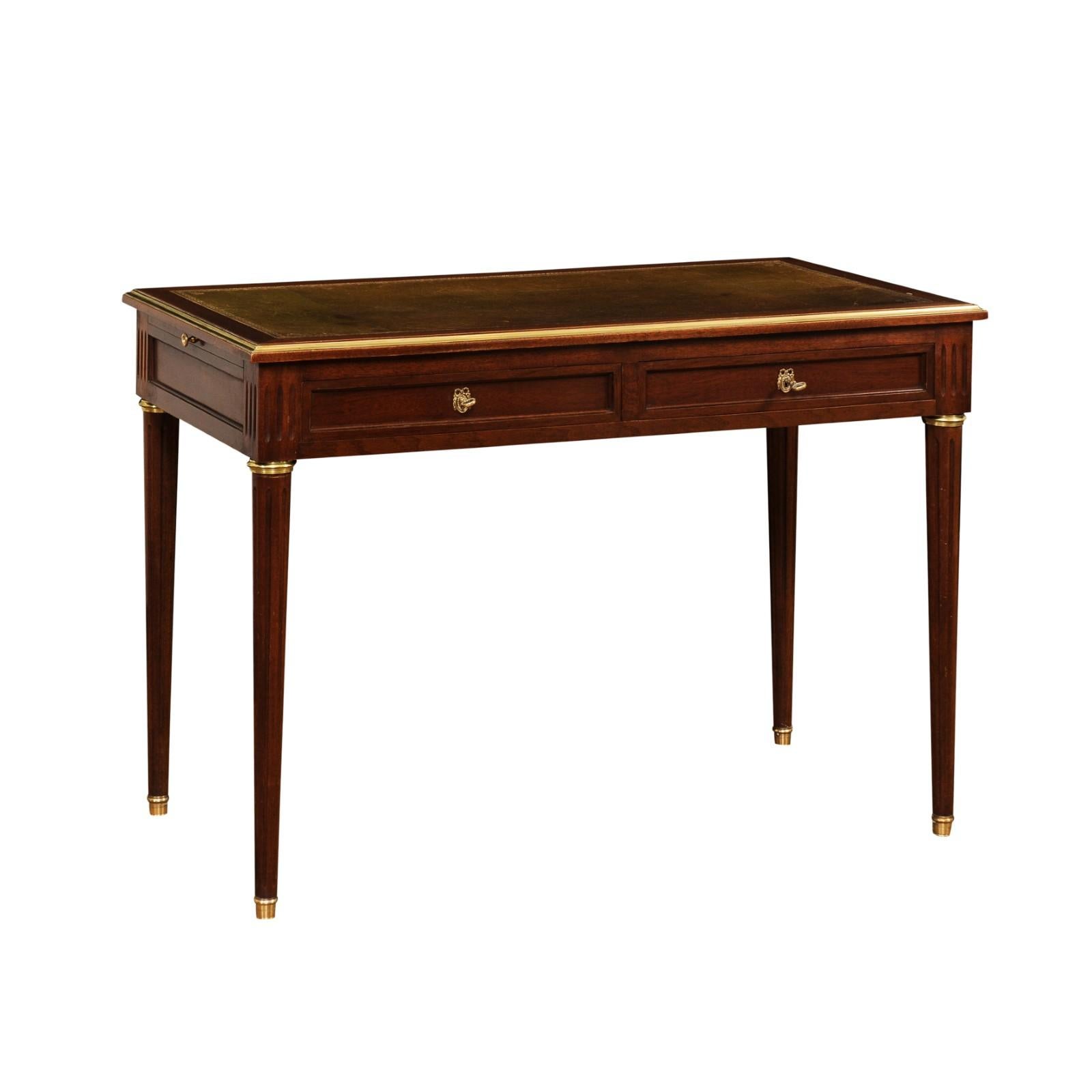 A French Louis XVI style mahogany and mahogany veneer desk from the early 20th century, with olive leather top, two drawers, lateral pull-outs and cylindrical legs on bronze feet. Created in France during the Turn of the Century, this Louis XVI