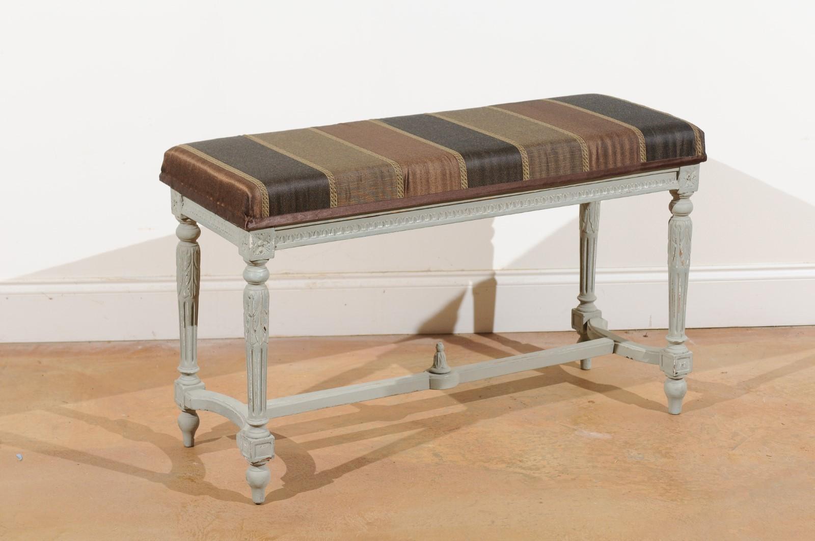 A French Louis XVI style two-seat painted piano bench from the early 20th century, with new upholstered top, fluted legs and cross stretcher. This French piano bench features a rectangular seat, upholstered with an exquisite brown and black fabric,